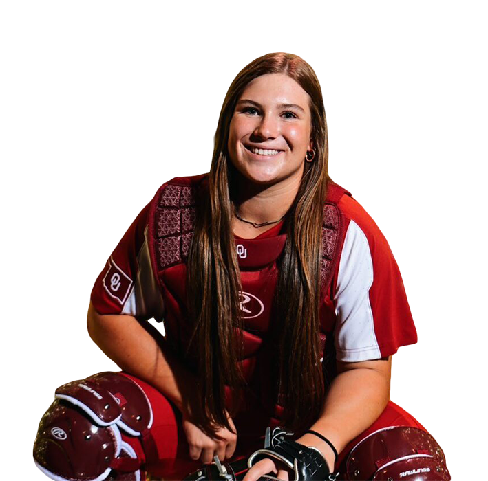 A smiling female football player in a red and white uniform sitting with her helmet and gloves in front of a black background.