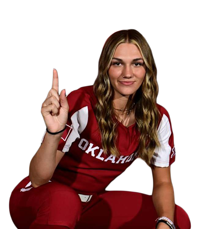 A young woman wearing a red and white Oklahoma Sooners sports jersey and red pants, sitting and pointing upward with her index finger.