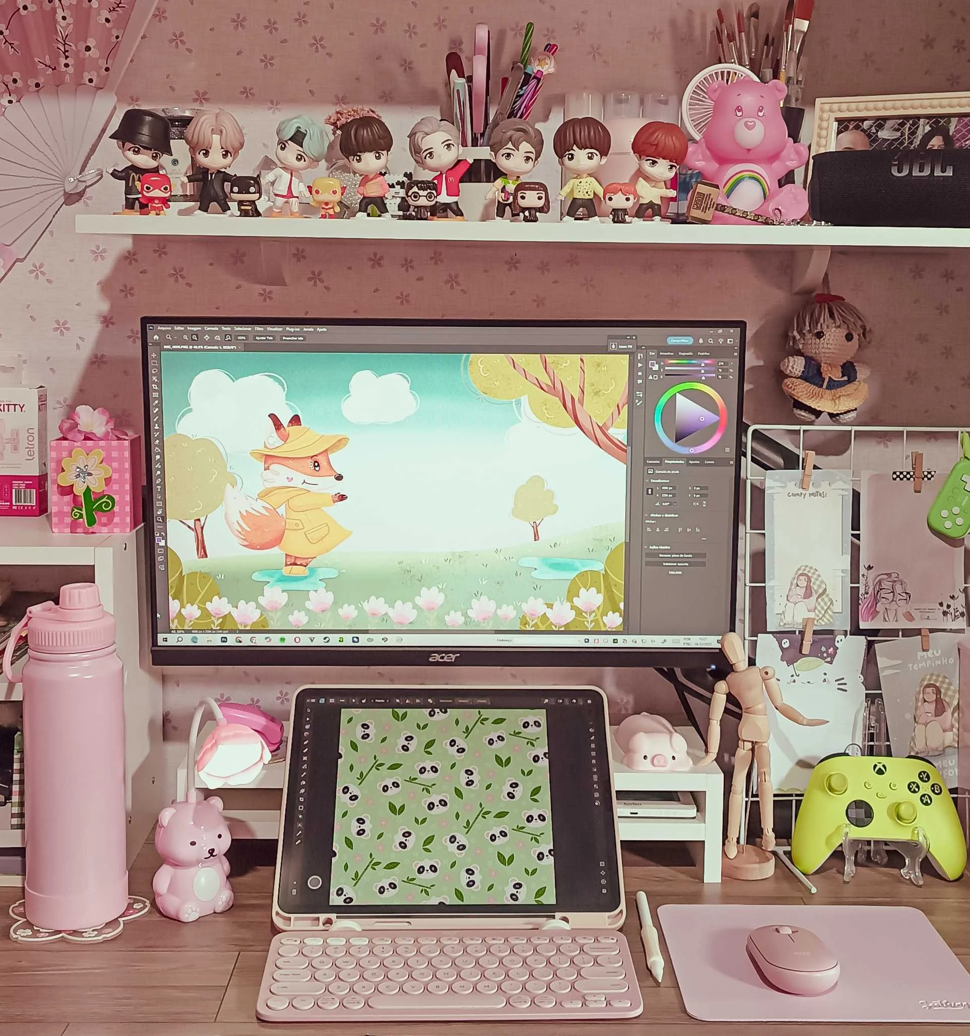 A workspace with a computer monitor displaying a cartoon fox in a yellow coat and hat, with a tree and flowers background; a tablet with panda and leaf pattern; pink water bottle, bunny figurine, and a pink lamp on the desk; shelves with plush toys, figurines, and stationery; and various decorative items and art supplies.