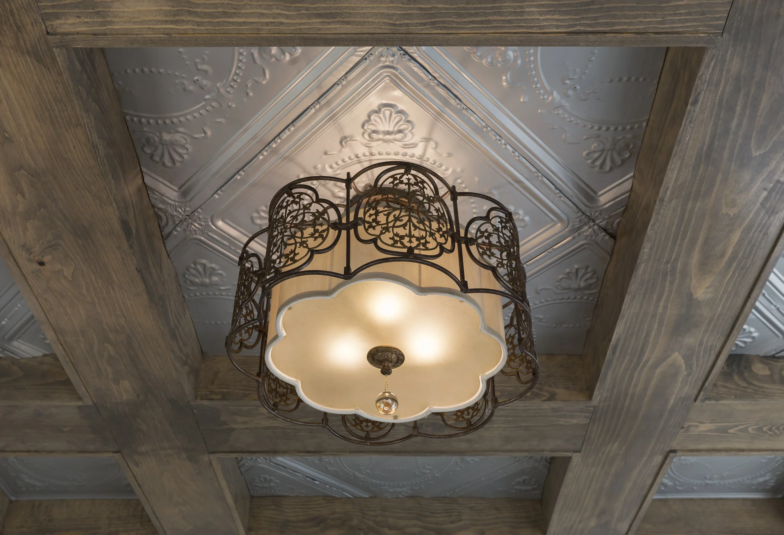 Ceiling with decorative tin tiles, wooden beams, and a hanging metal and fabric lampshade.