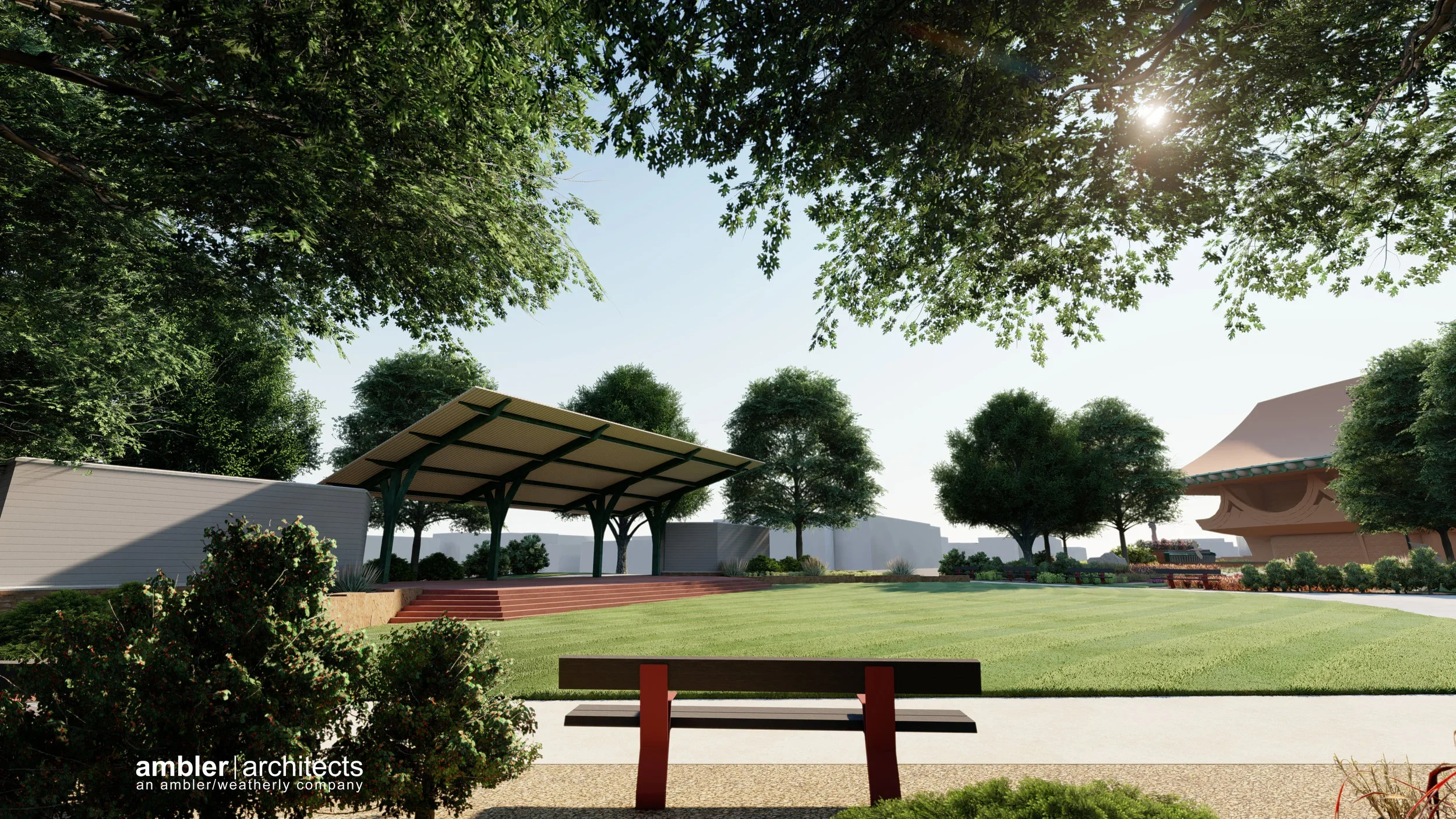 A park with a grassy area, trees, benches, a stage with a roof, and a walking path, with the sun shining through the trees.