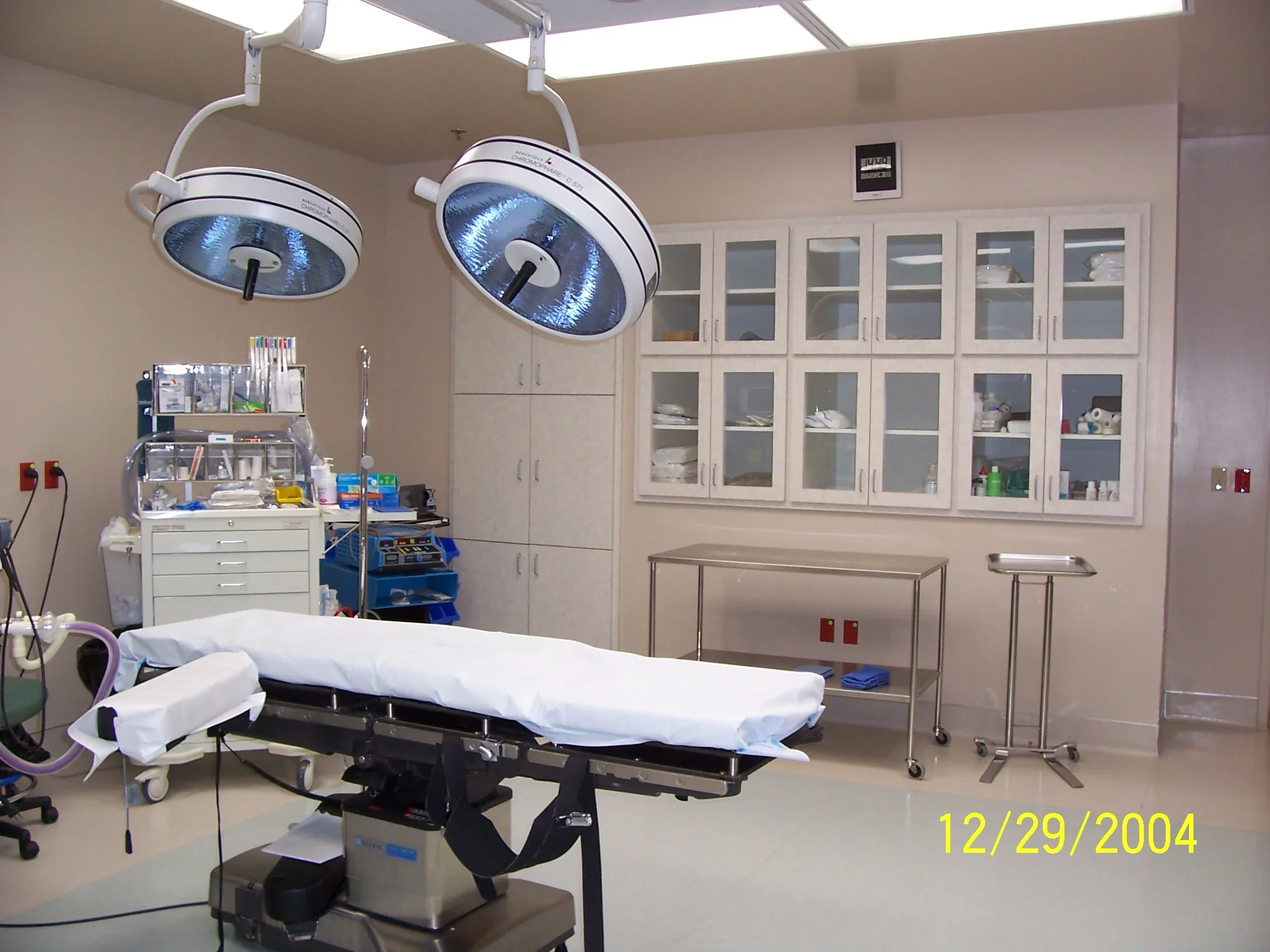 An empty operating room with surgical lights overhead, an operating table, and medical cabinets with supplies.