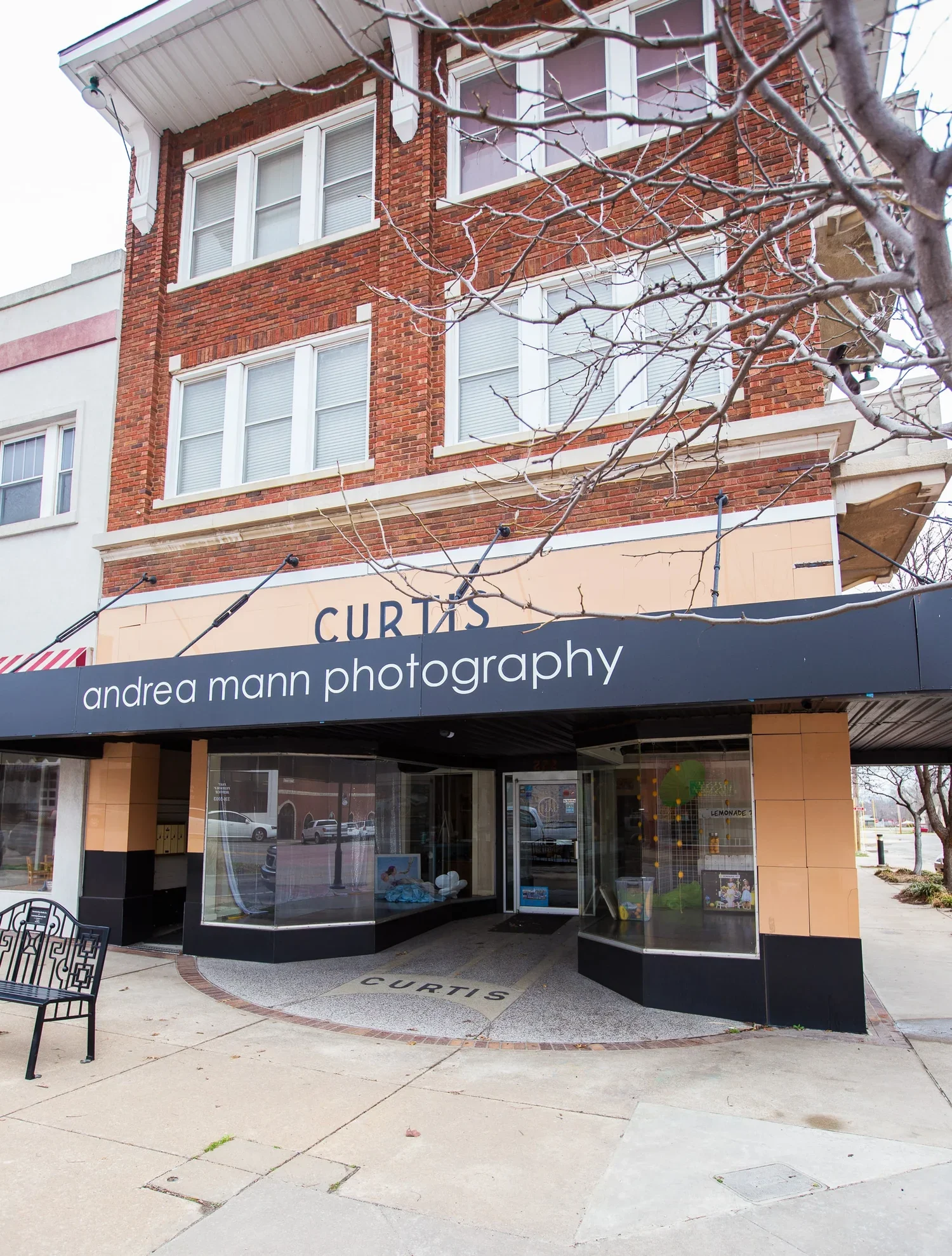 Street view of Curtis Lofts with a photography studio called Andrea Mann Photography on the ground floor, with a black awning, large windows, and a sidewalk in front.