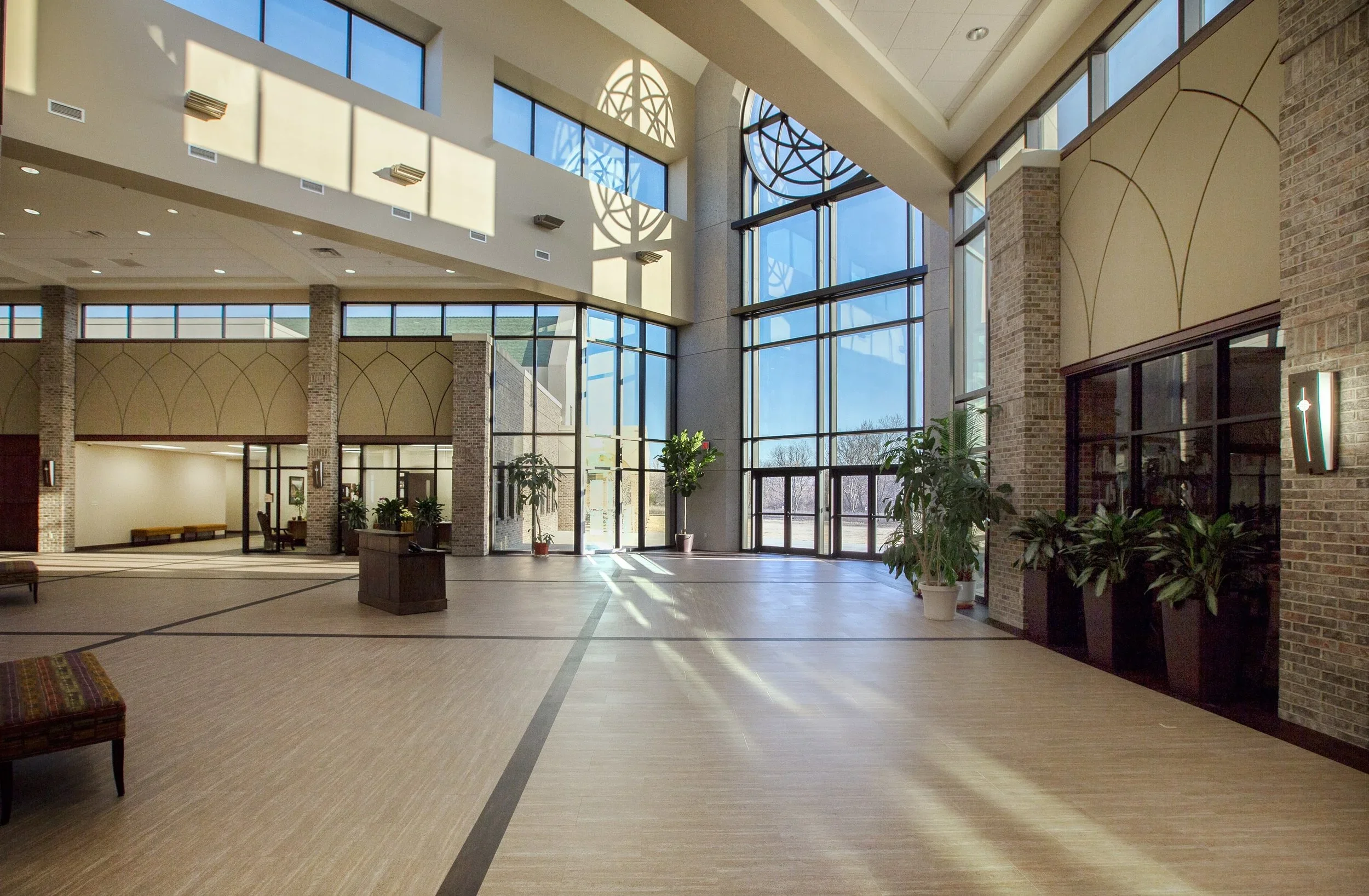  spacious lobby area with large windows, potted plants, and seating, illuminated by natural sunlight.