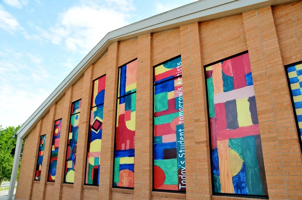 Colorful abstract mural on the side of a brick building with vertical panels and a partially visible message.