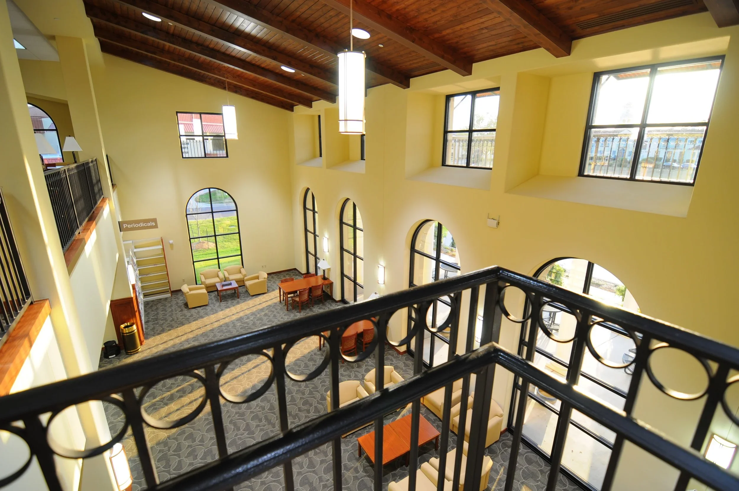 Interior view of a multi-story building's lobby with high ceilings, large windows, a balcony, and seating area with sofas and tables.