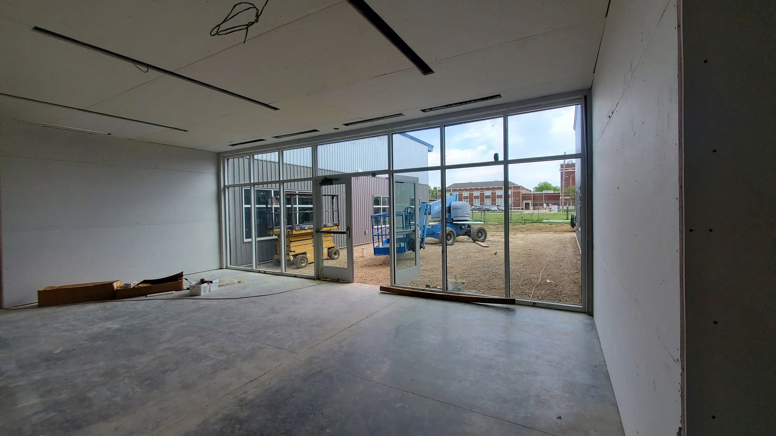 Interior of a building under construction with large glass windows showing construction equipment outside.