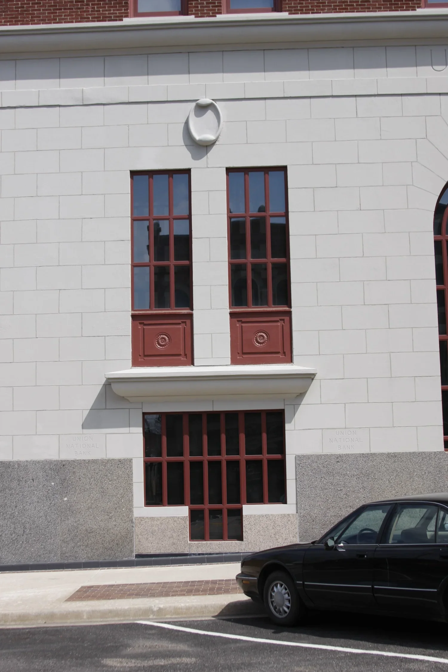 Facade of a building with red-framed windows, decorative white architectural details, and a small black car parked in front.