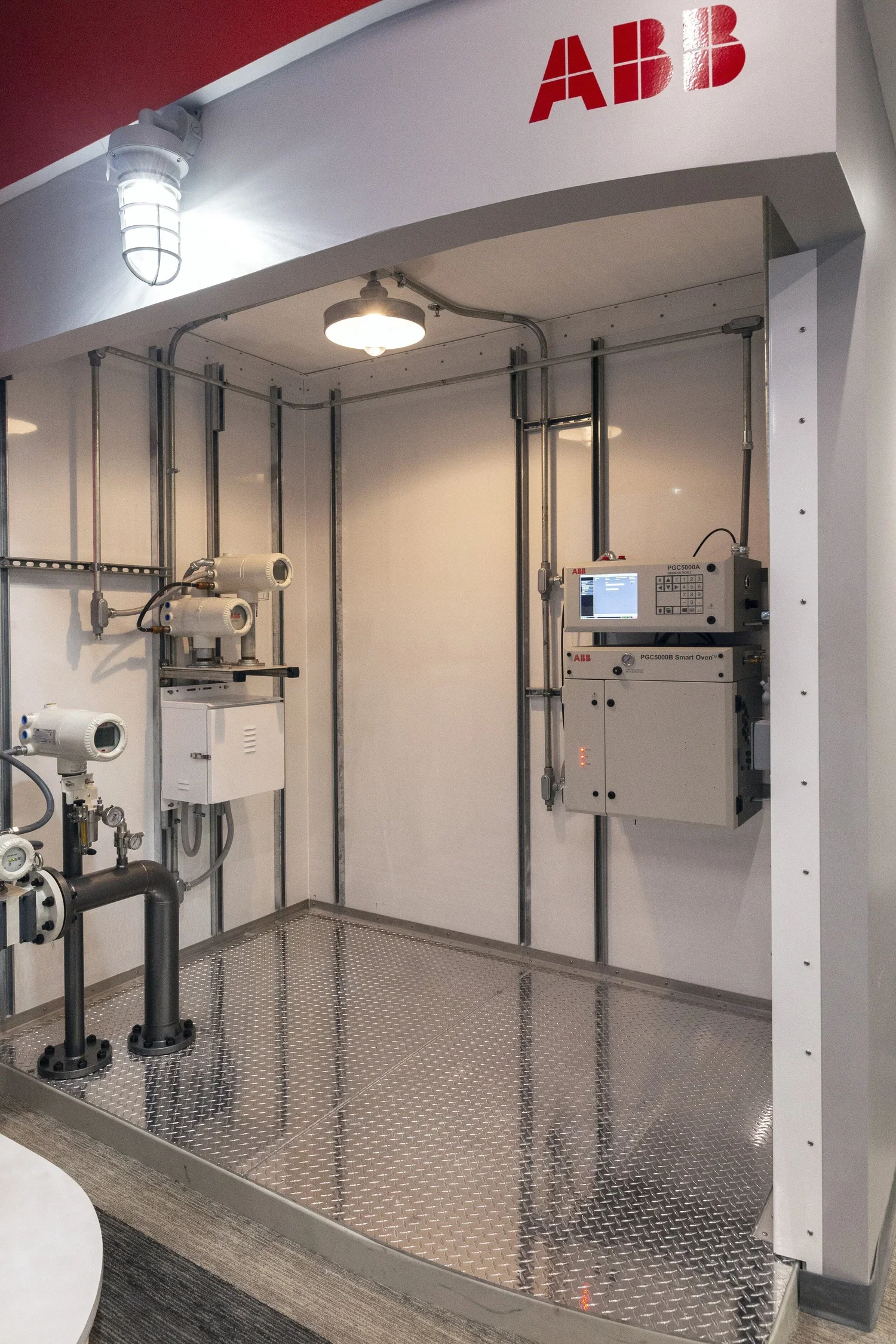Empty enclosed equipment room with industrial piping and ABB control panels, Industrial light fixtures, metal floor, and white walls.