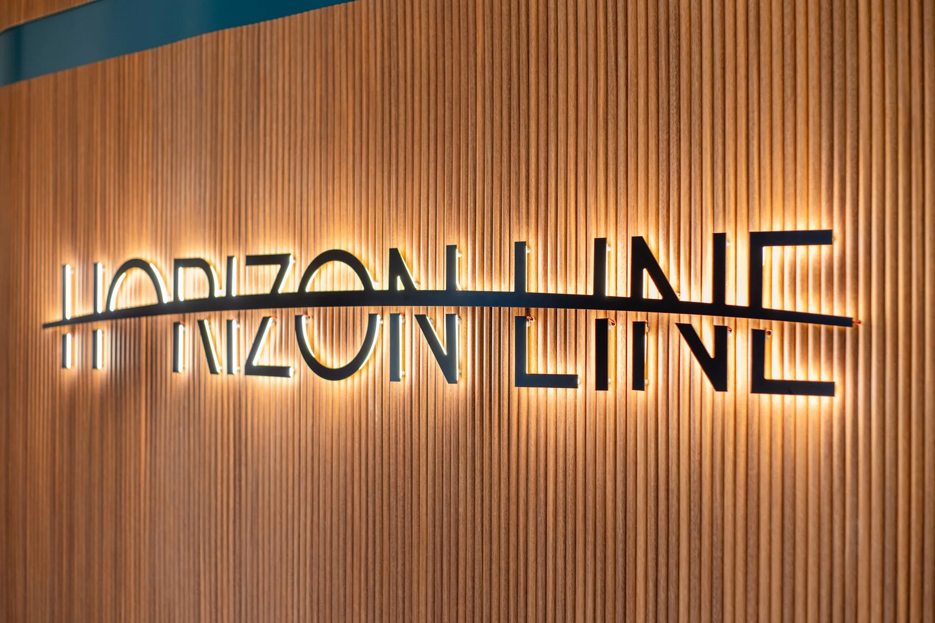 Backlit sign reading 'HORIZON LINE' mounted on a wooden slat wall.