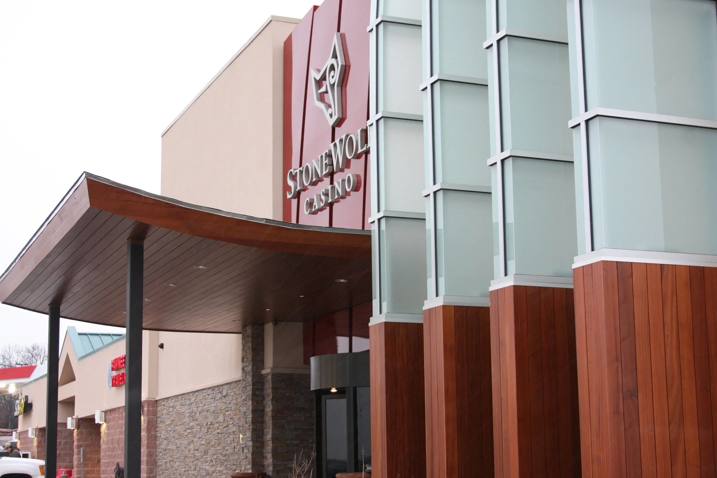 Exterior view of Stonewolf Casino showing entrance with a large sign, modern architectural design with glass windows, stone and wood accents.