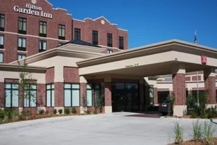 Exterior view of a Hilton Garden Inn hotel with a brick facade, covered entrance, and blue sky