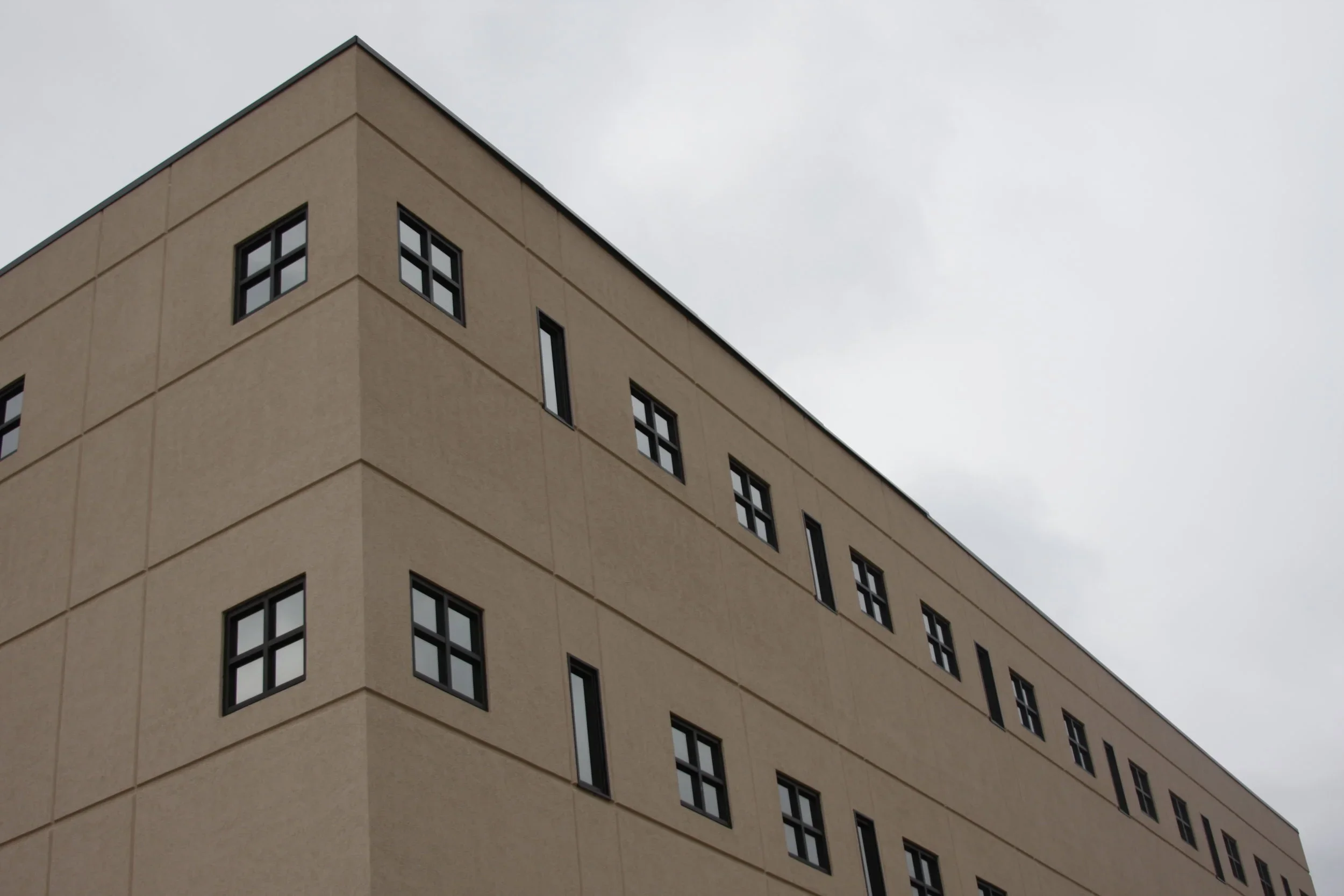 A beige multi-story building with black-framed windows on a cloudy sky day.