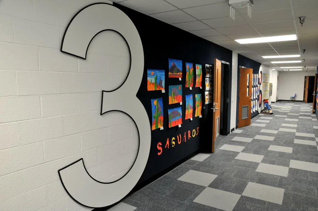 School hallway with artwork display and a large number 3 on the wall.