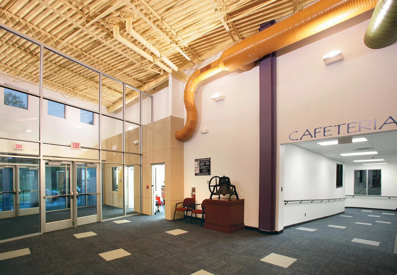 Interior of a school lobby, showing entrance doors, a hallway with handrails, and a sign for the cafeteria.