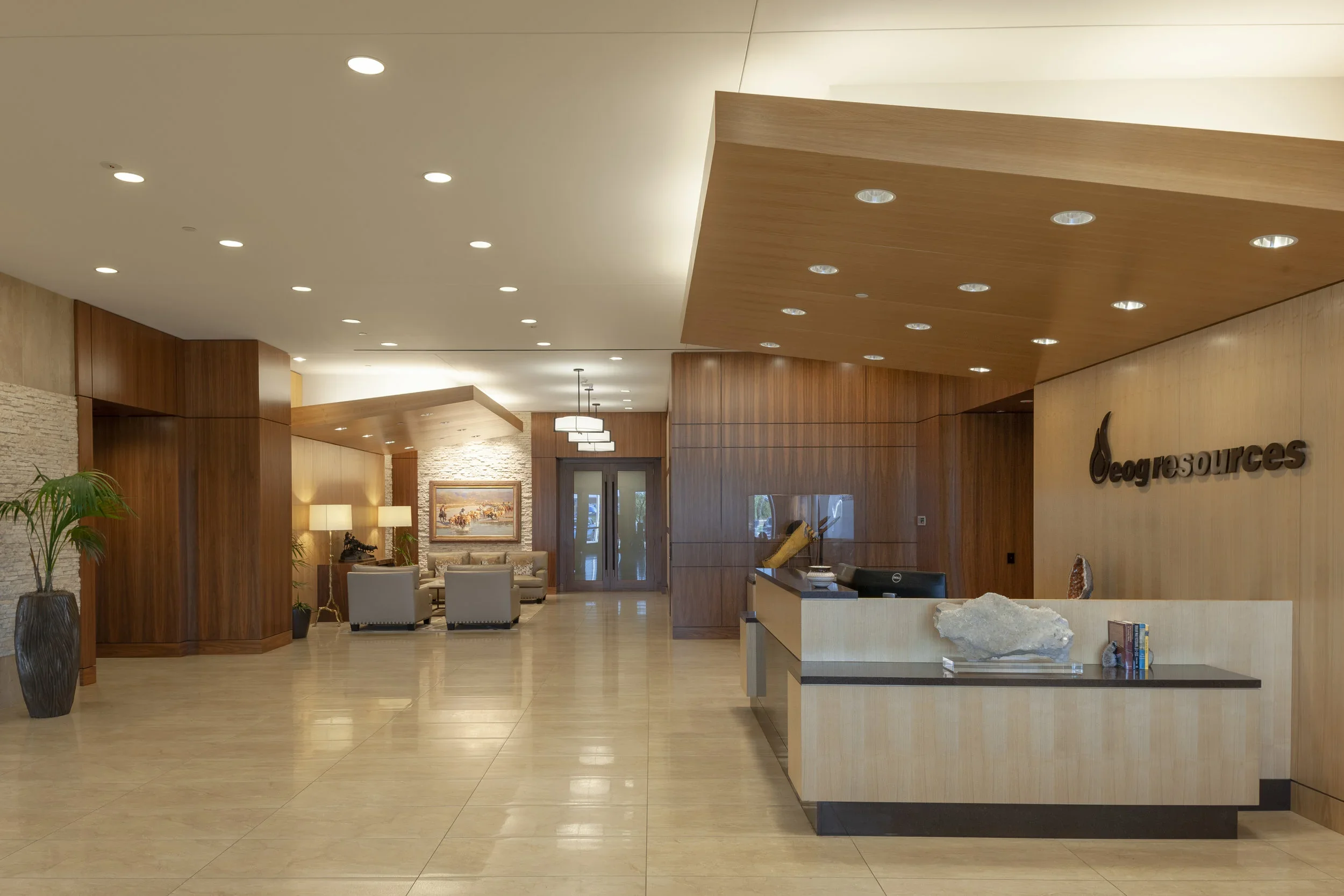 Main Lobby of EOG Midland Headquarters Building II wooden and stone decor, seating area with sofas, reception desk with decorative rocks and books, and the sign 'Oegresources' on the wall.