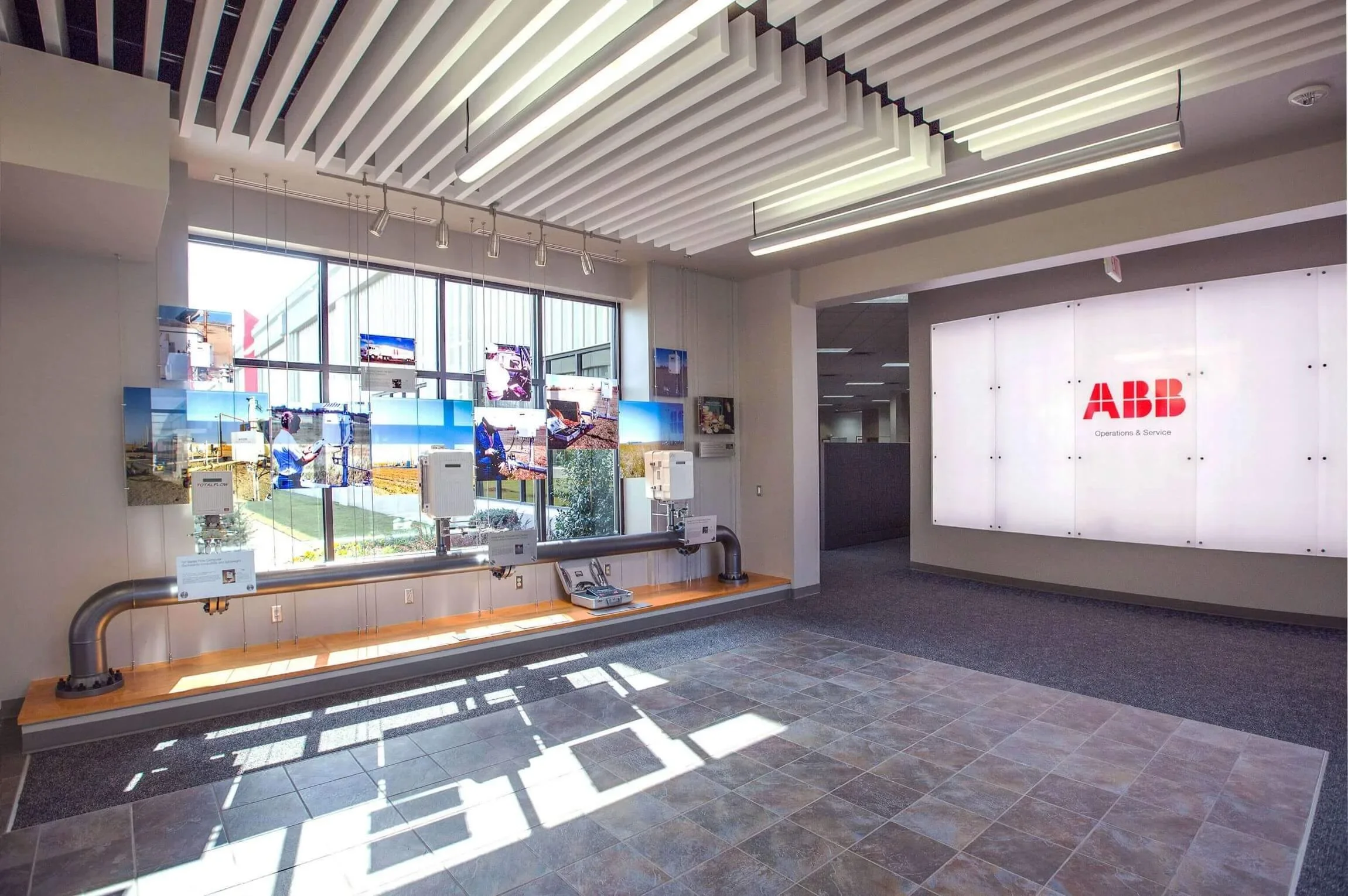 ABB Operations & Service office lobby with large illuminated white wall and company logo and windows displaying industrial scenes and a mannequin dressed in a lab coat.