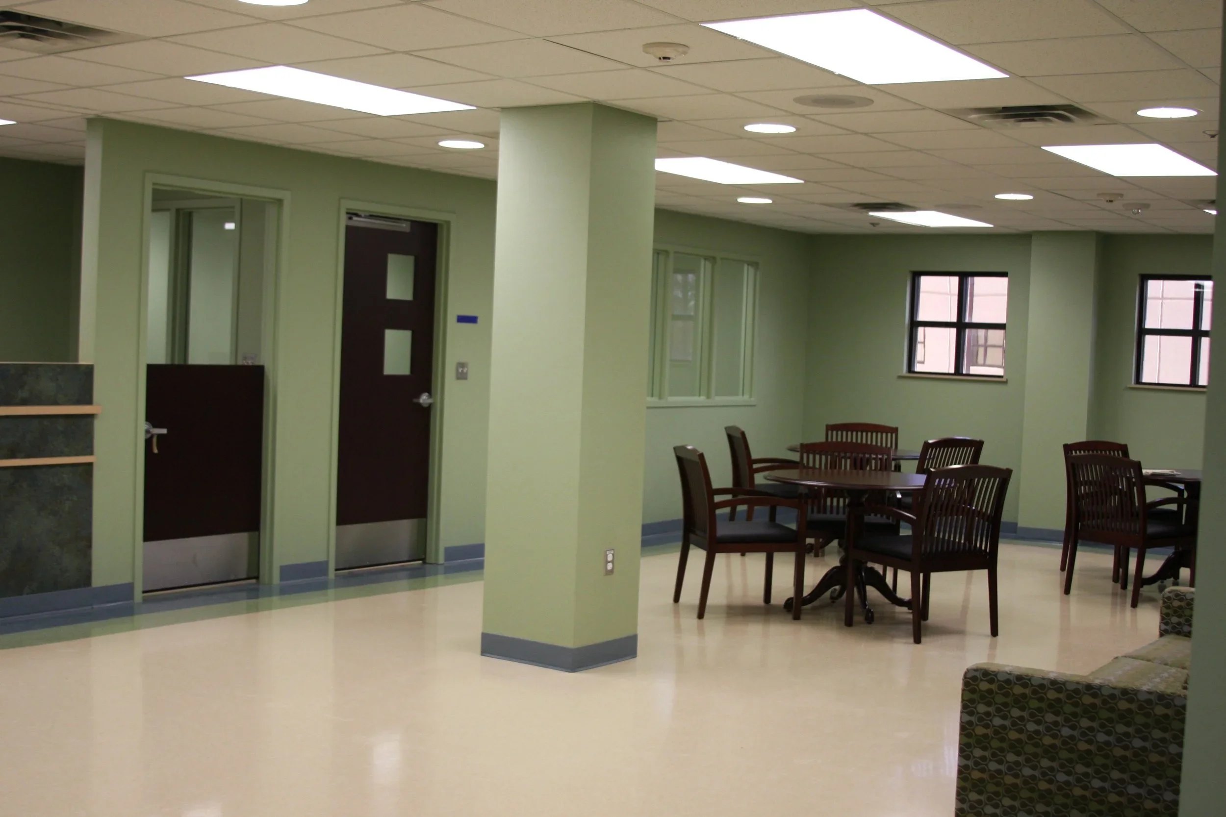 Interior view of a room with green walls, a round wooden table surrounded by six chairs, windows, and two closed doors.