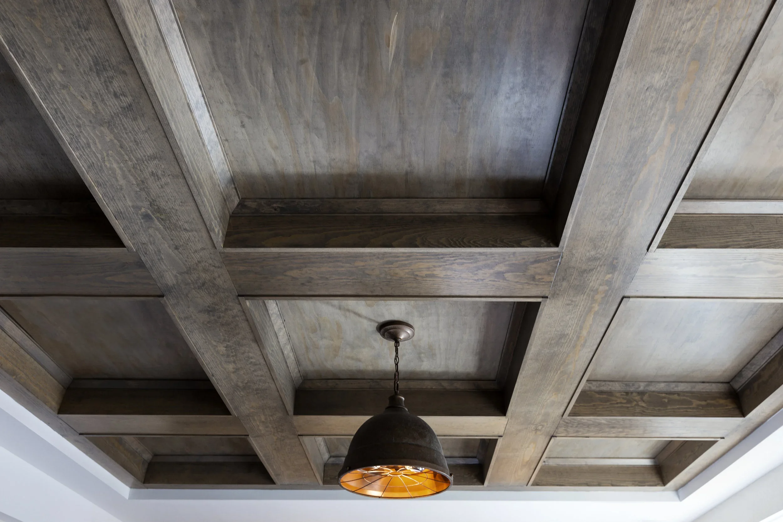Wooden ceiling with a grid pattern and a hanging metal light fixture with an orange interior.