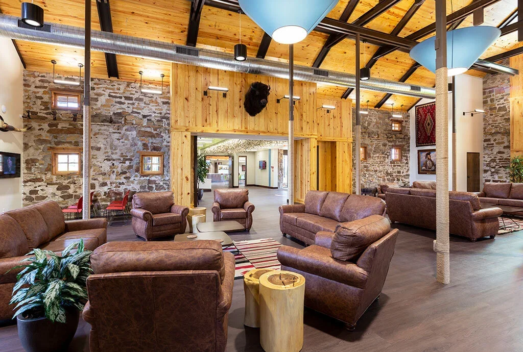 Lobby area with leather sofas, wooden accents, stone walls, and large light fixtures in a rustic style.