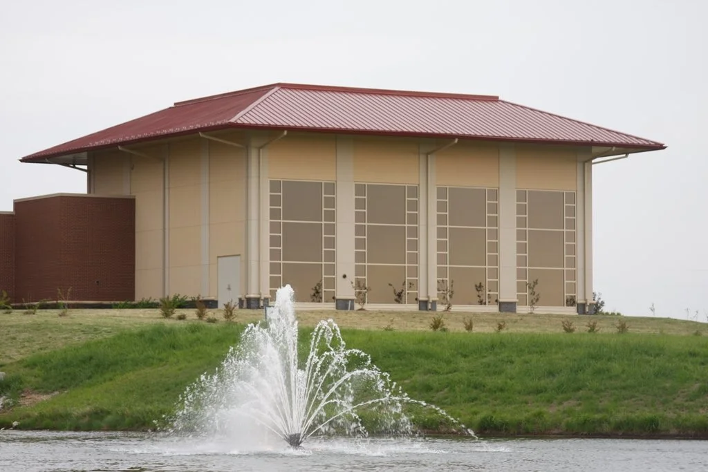 Exterior view of Bailey Medical Center Education Building in Owasso, OK with a red metal roof situated behind a grassy area with a water fountain in the foreground.