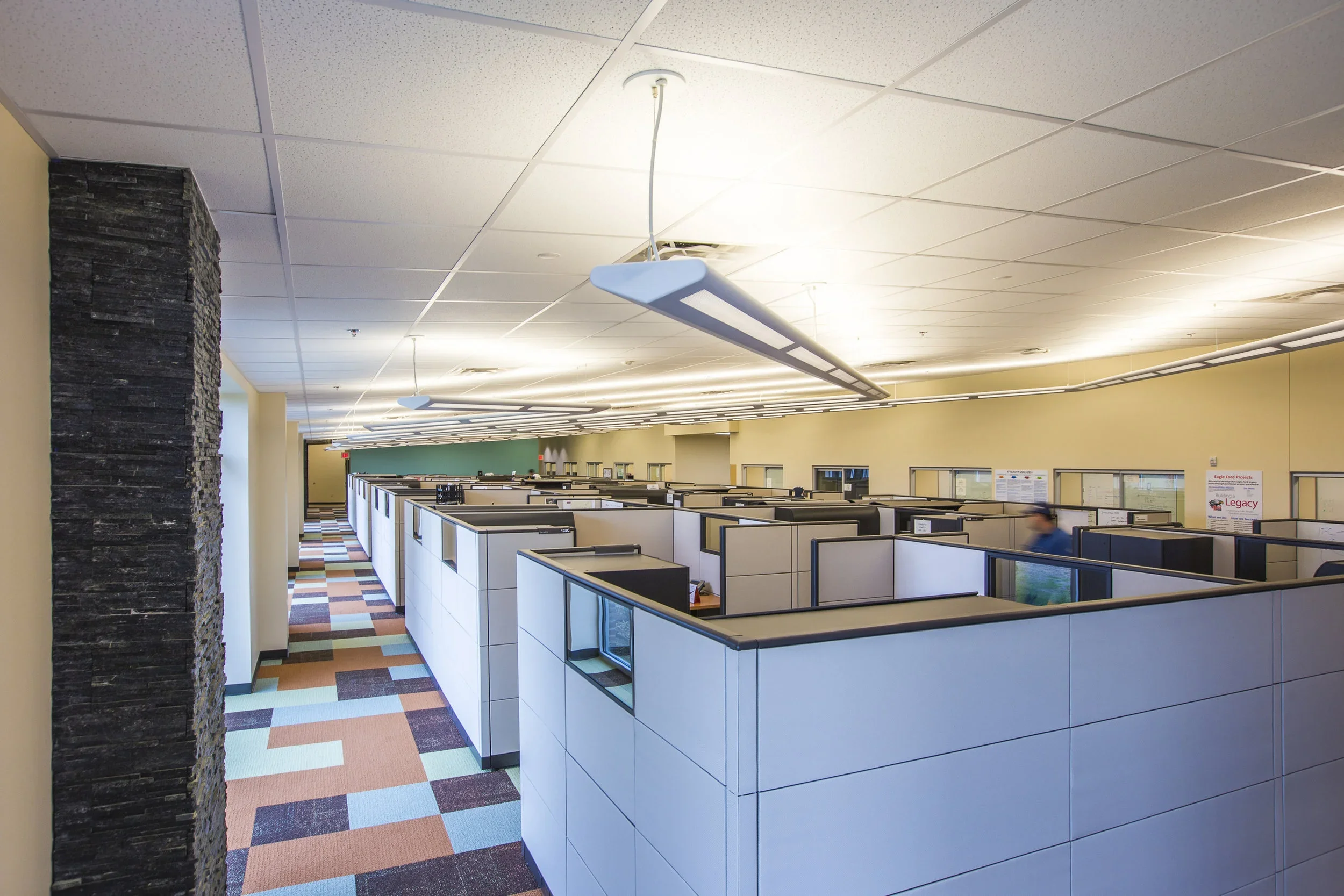 Empty office cubicles with a colorful carpet and modern lighting fixtures.