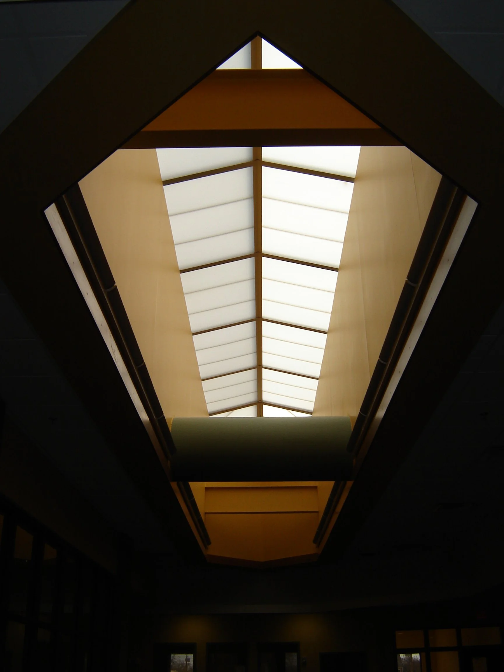 Looking up at a skylight ceiling with a geometric design inside of First Baptist Church Family Life Center, featuring a large central rectangular opening and smaller surrounding sections, illuminated by natural light.