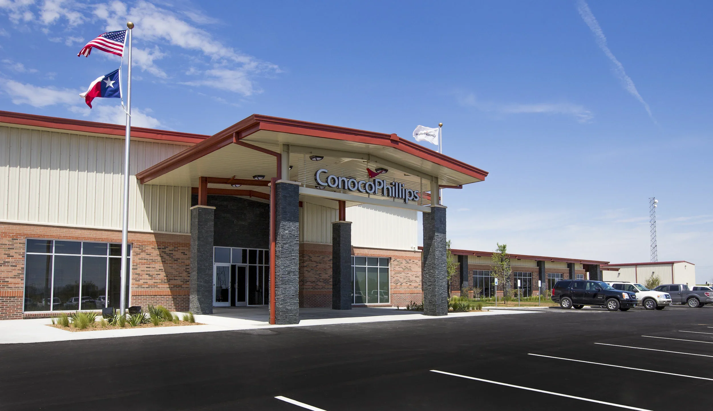 Exterior of a ConocoPhillips office building with three flags flying, including the American and Texas flags, under a clear blue sky.
