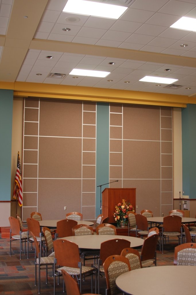 Inside of Bailey Medical Center Education Building's conference room with round tables and chairs, a podium with a microphone, a flower arrangement, and an American flag on a pole.