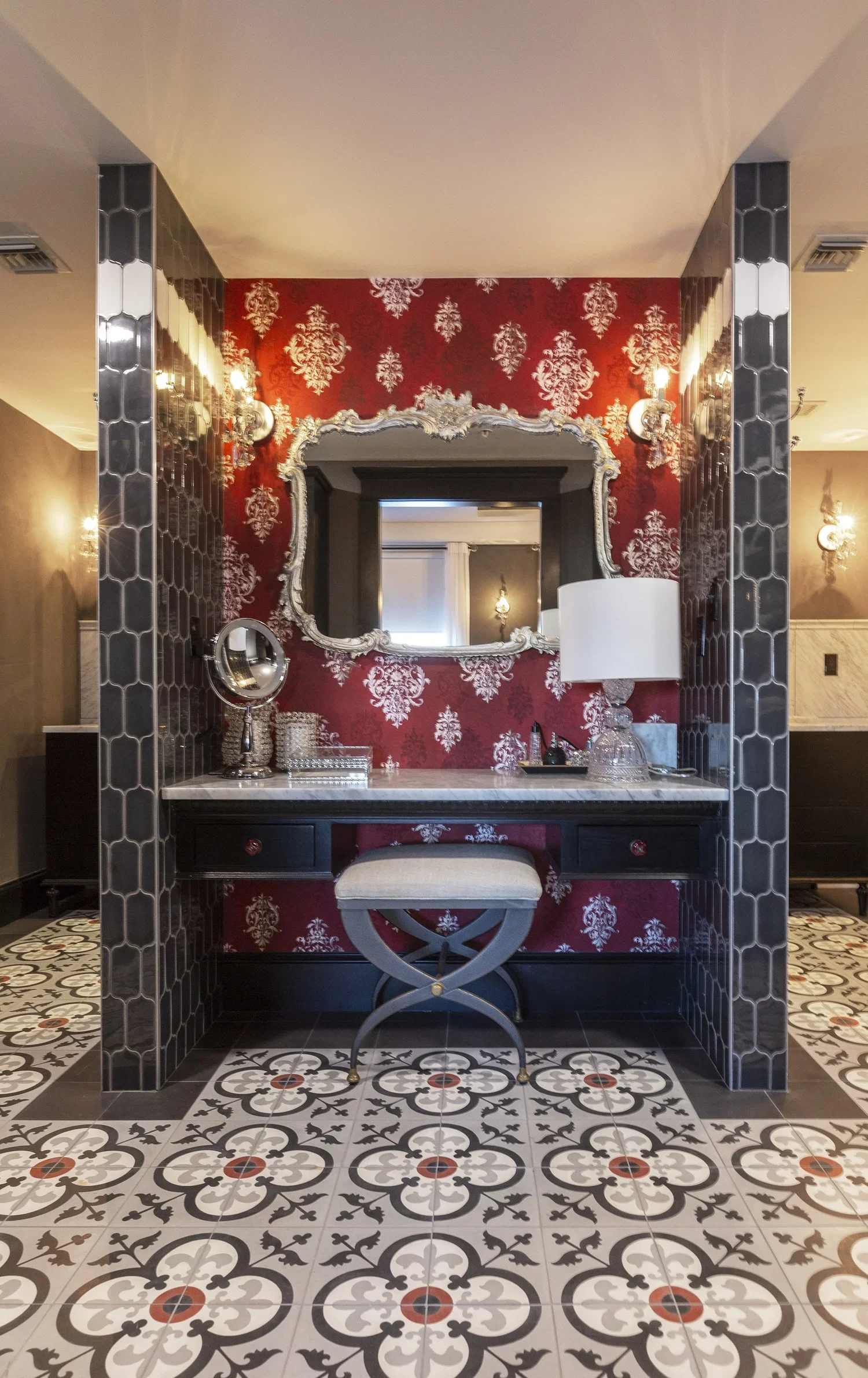 Elegant powder room with a black vanity, ornate mirror, white table lamp, decorative items, patterned tile floor, and red damask wallpaper.