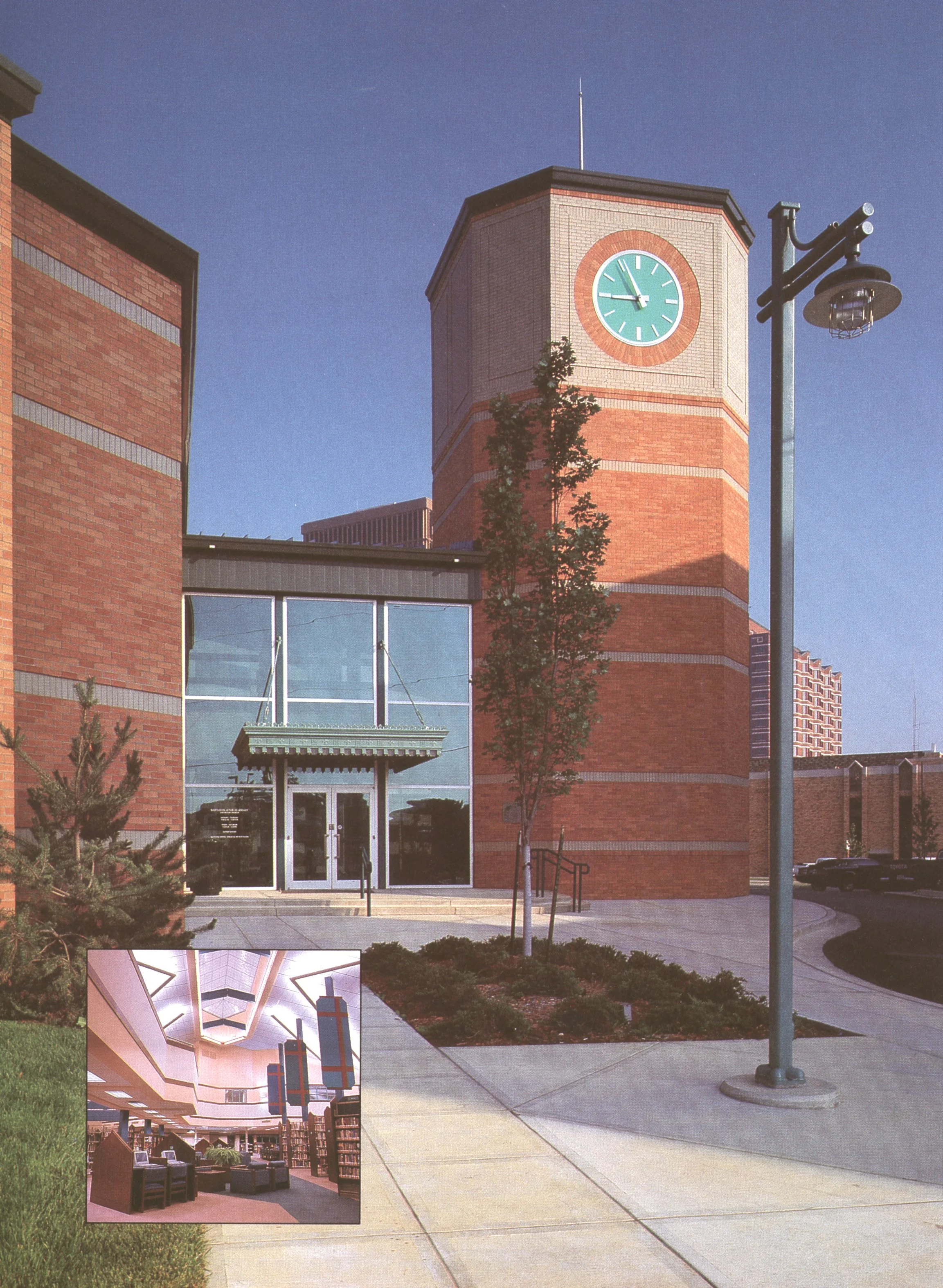 Exterior view of Bartlesville Public Library with a clock tower, a glass entrance, a lamppost, and trees in an outdoor plaza. An inset image shows a library interior with bookshelves, chairs, and bright lighting.