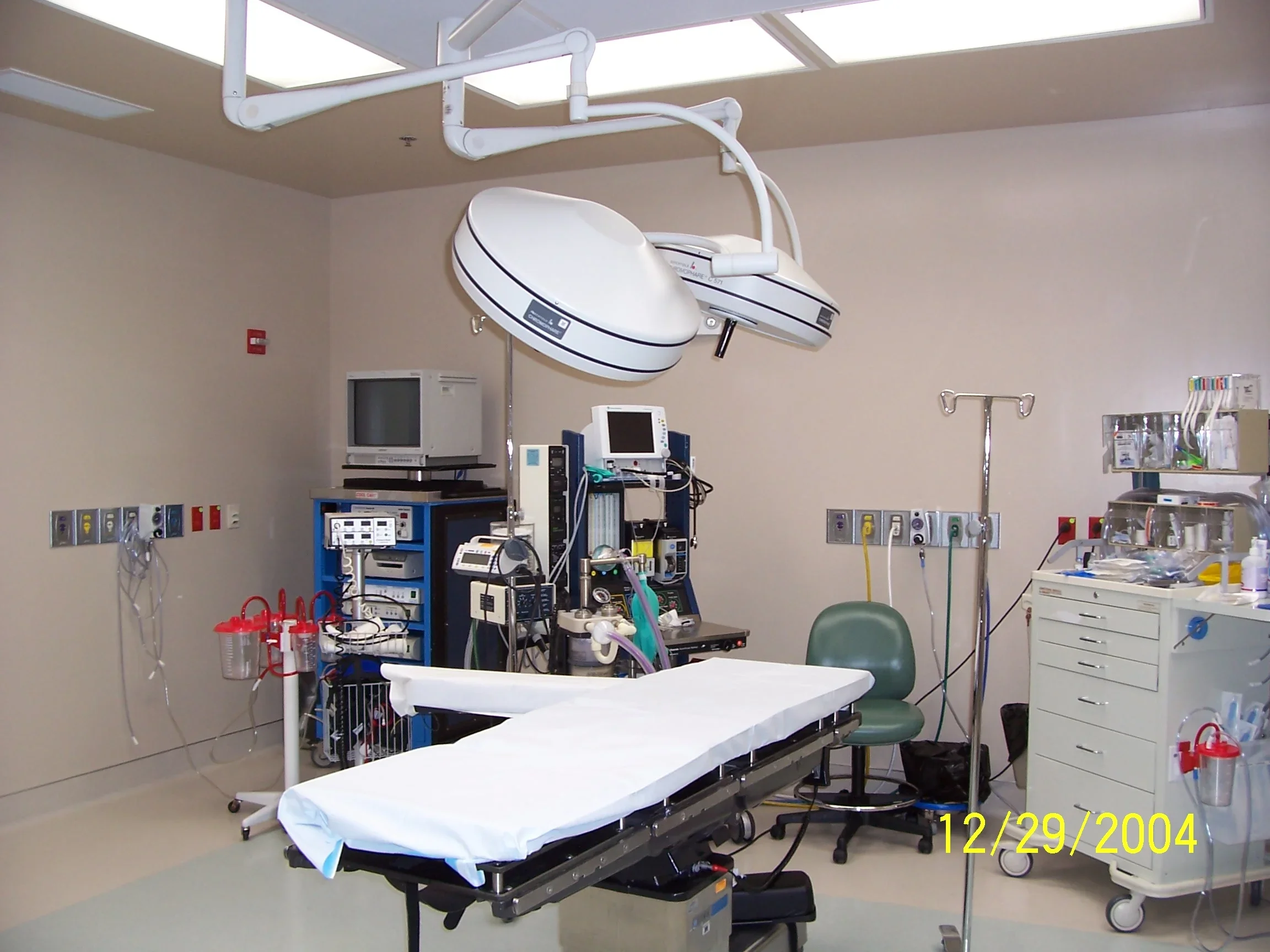 A hospital operating room with medical equipment, an operating table covered with a white sheet, monitors, IV poles, and cabinets with supplies.