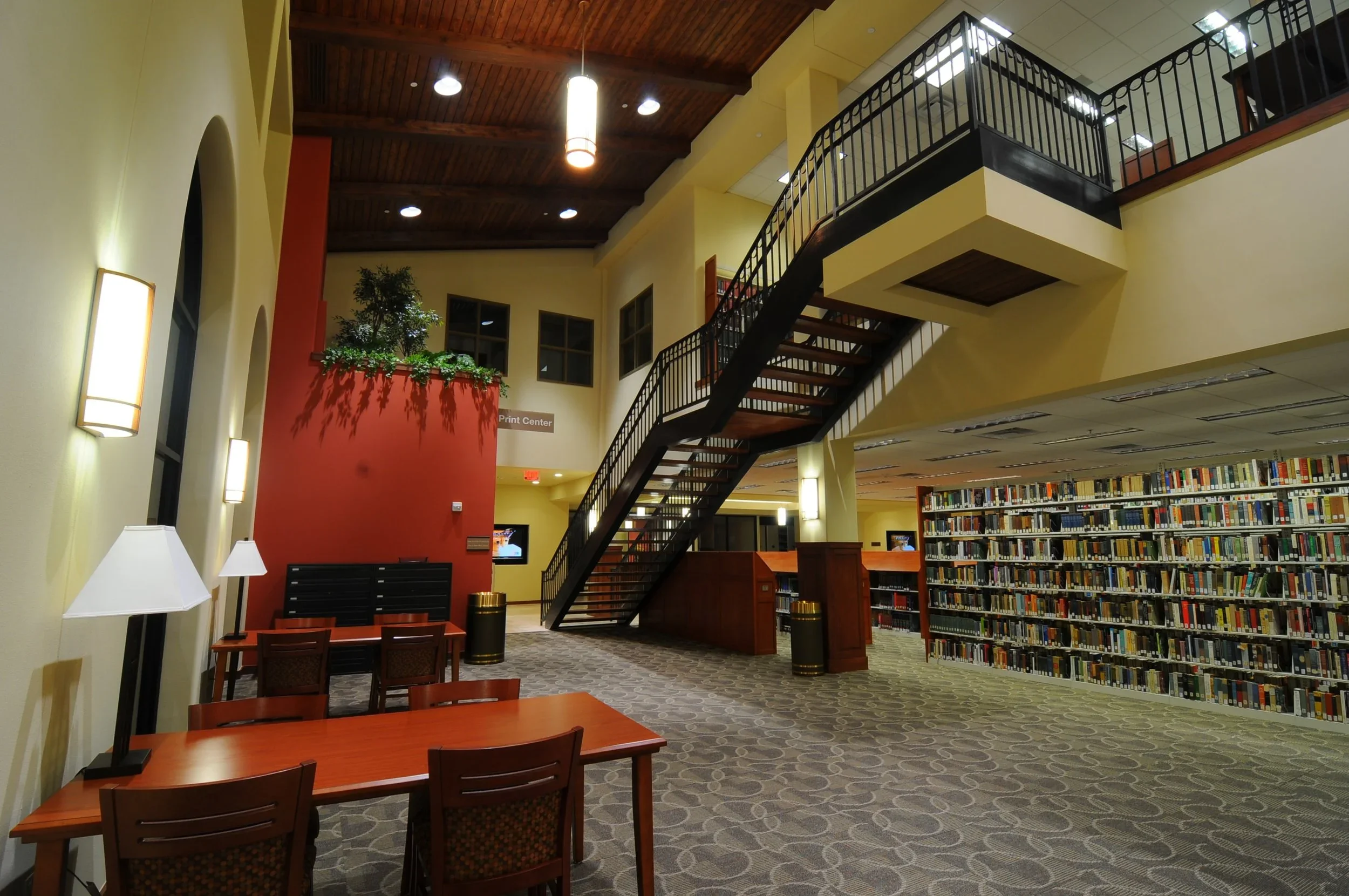 Interior of a library with bookshelves, a staircase, and seating areas.