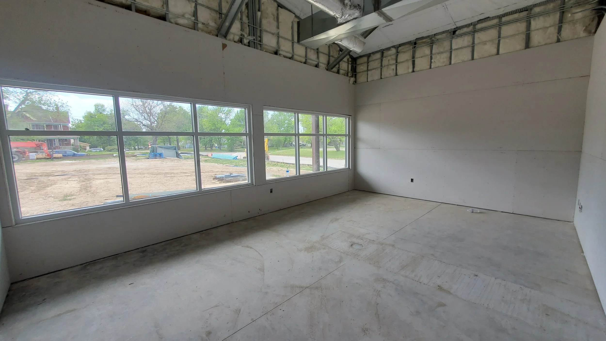 Interior of a room under construction with large windows and unfinished walls and ceiling.