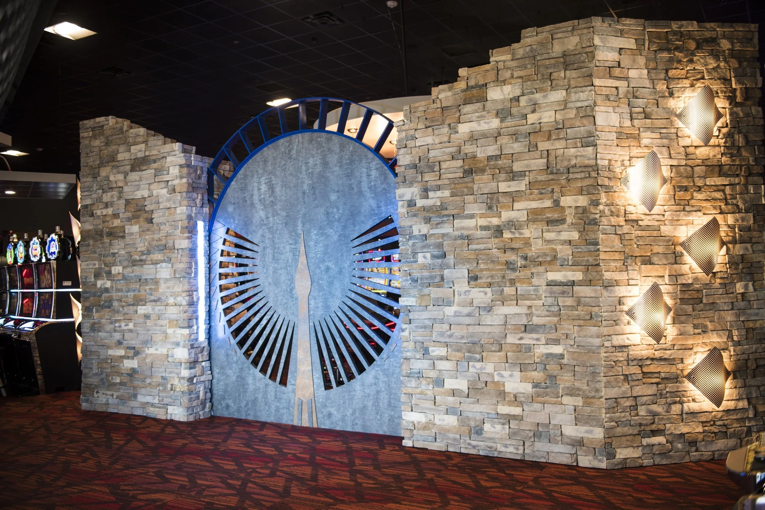 Slot machines in a casino with a brick wall and a large clock sculpture in the background.