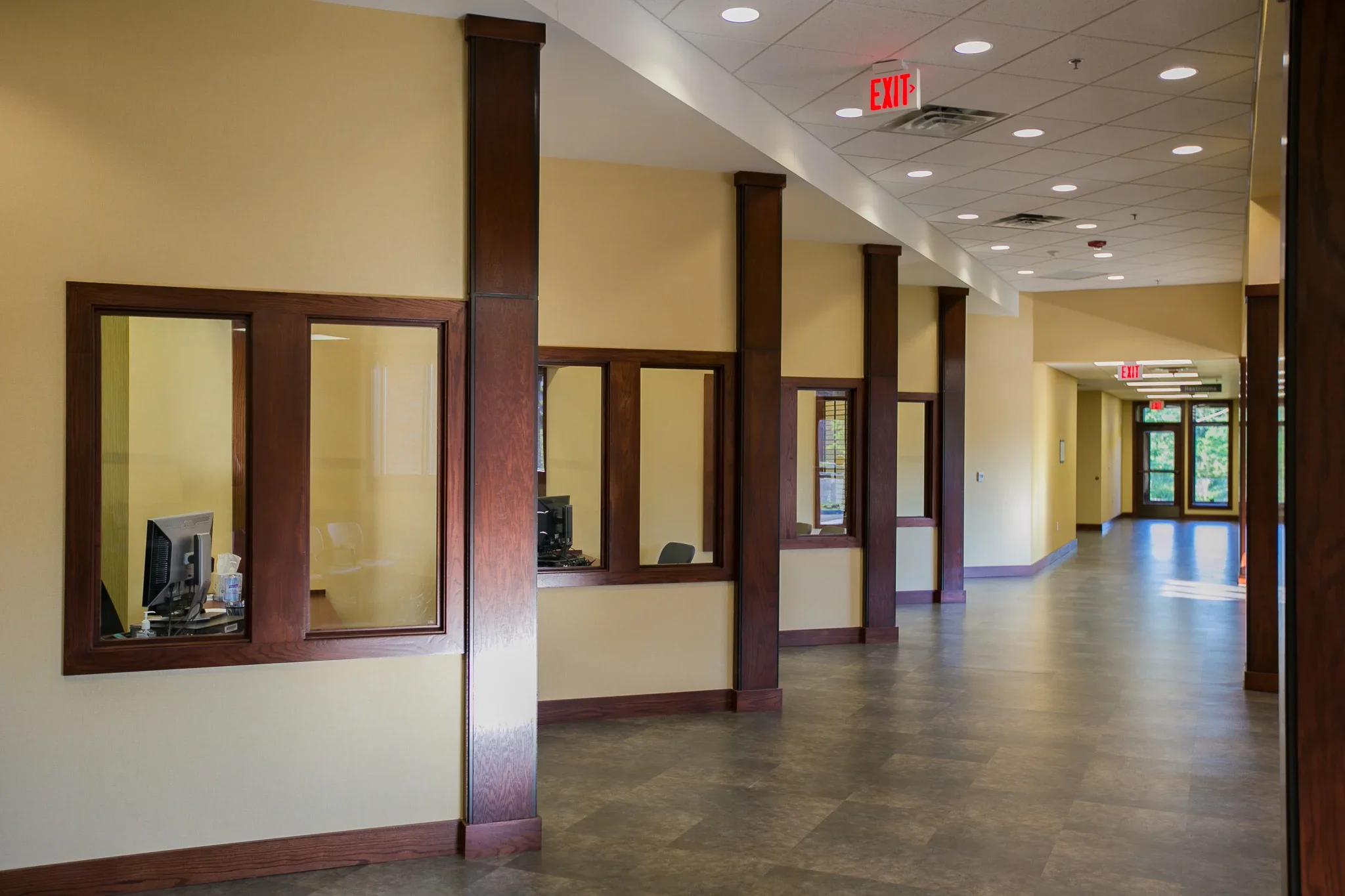 Empty reception area with yellow walls, wooden accents, and a hallway leading to glass doors with natural light.