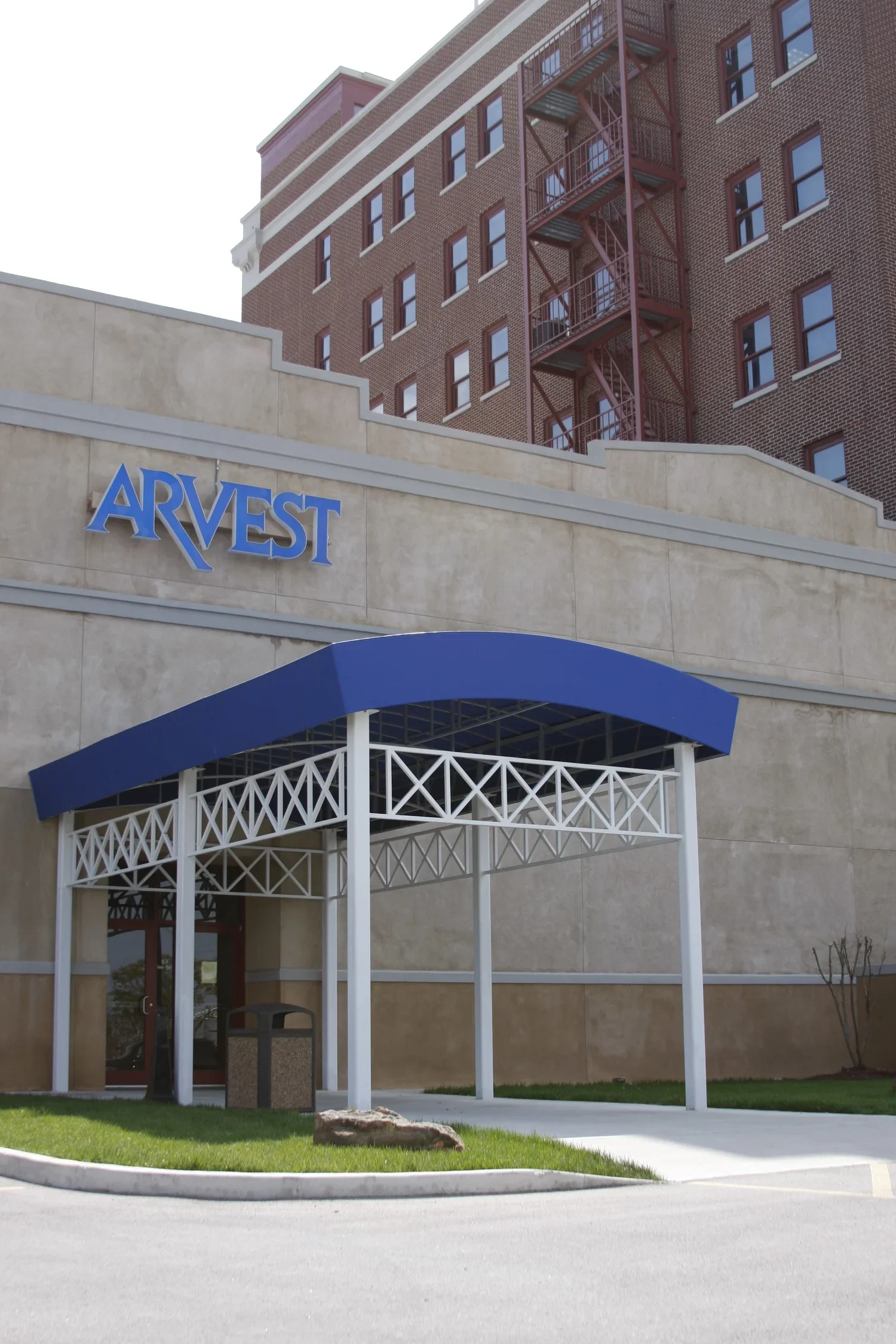 Building with a sign that reads 'ARVEST' and a blue awning over a sidewalk entrance.