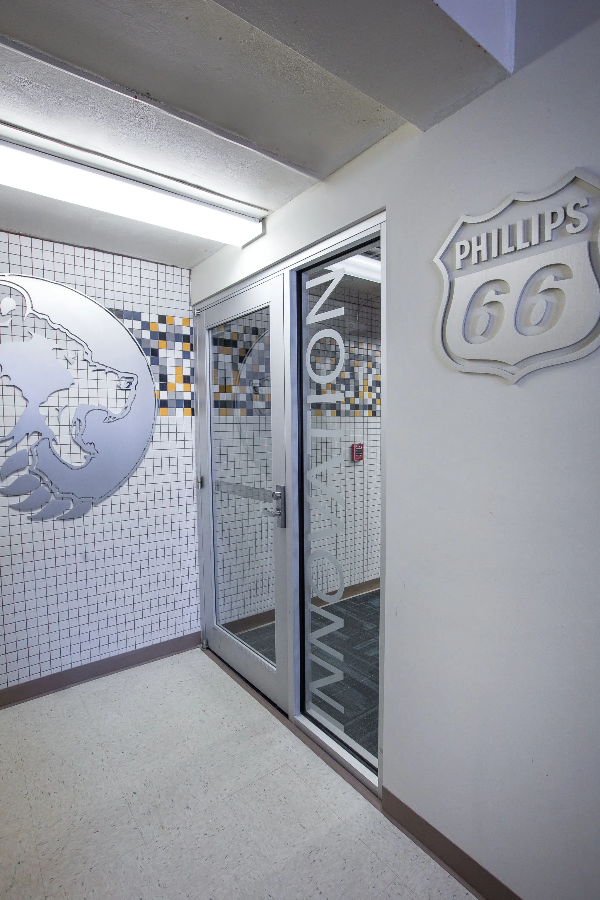 Entrance to a room with glass door and a Route 66 sign on a white wall. Decorative globe and mosaic tile artwork on the wall.