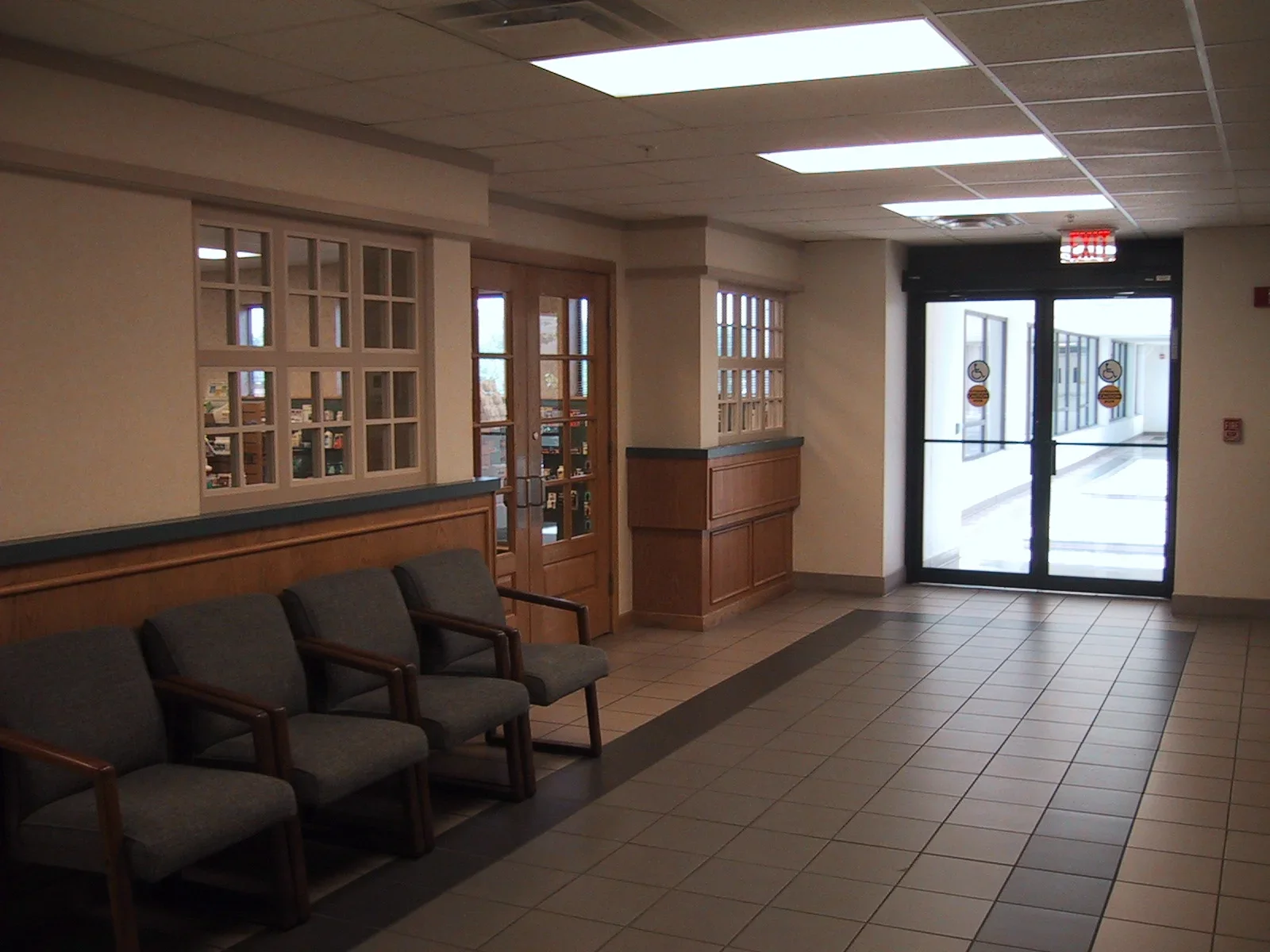 Empty waiting area with chairs, wood paneling, glass doors, and an exit door in a public building.