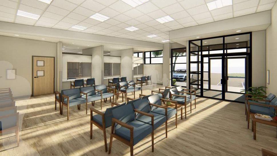 A spacious waiting area with rows of blue chairs, large glass doors leading outside, and a reception desk in the background.