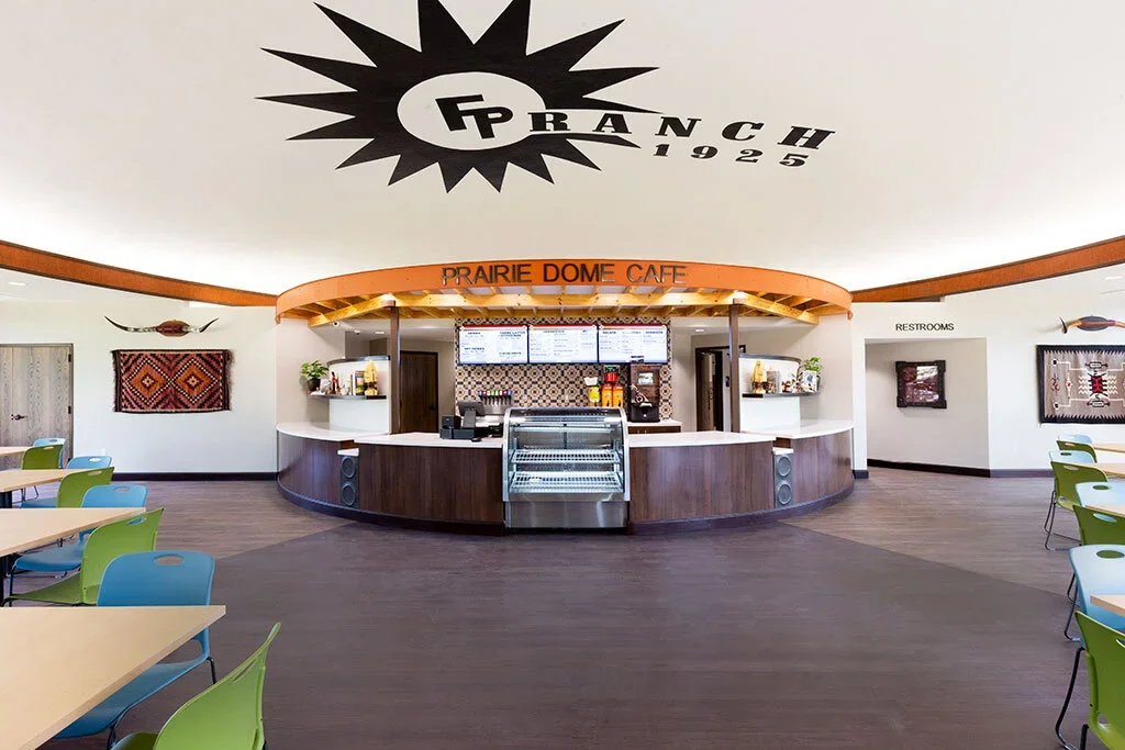 Interior of Prairie Dome Cafe with a curved counter, digital menu boards, and colorful chairs in the seating area.