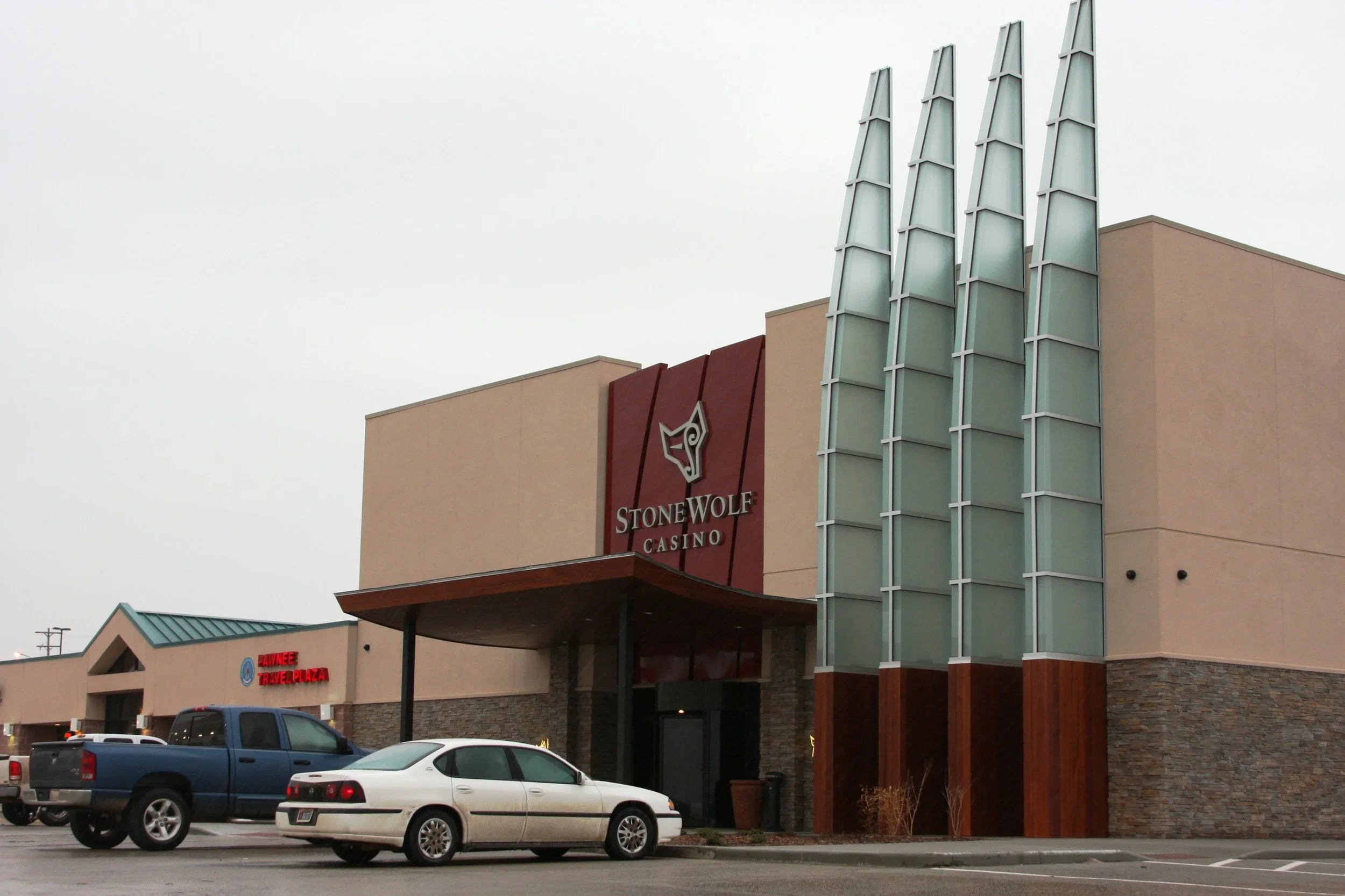 Stonewolf Casino building with beige and red exterior, glass architectural features, and parking lot with cars in front.