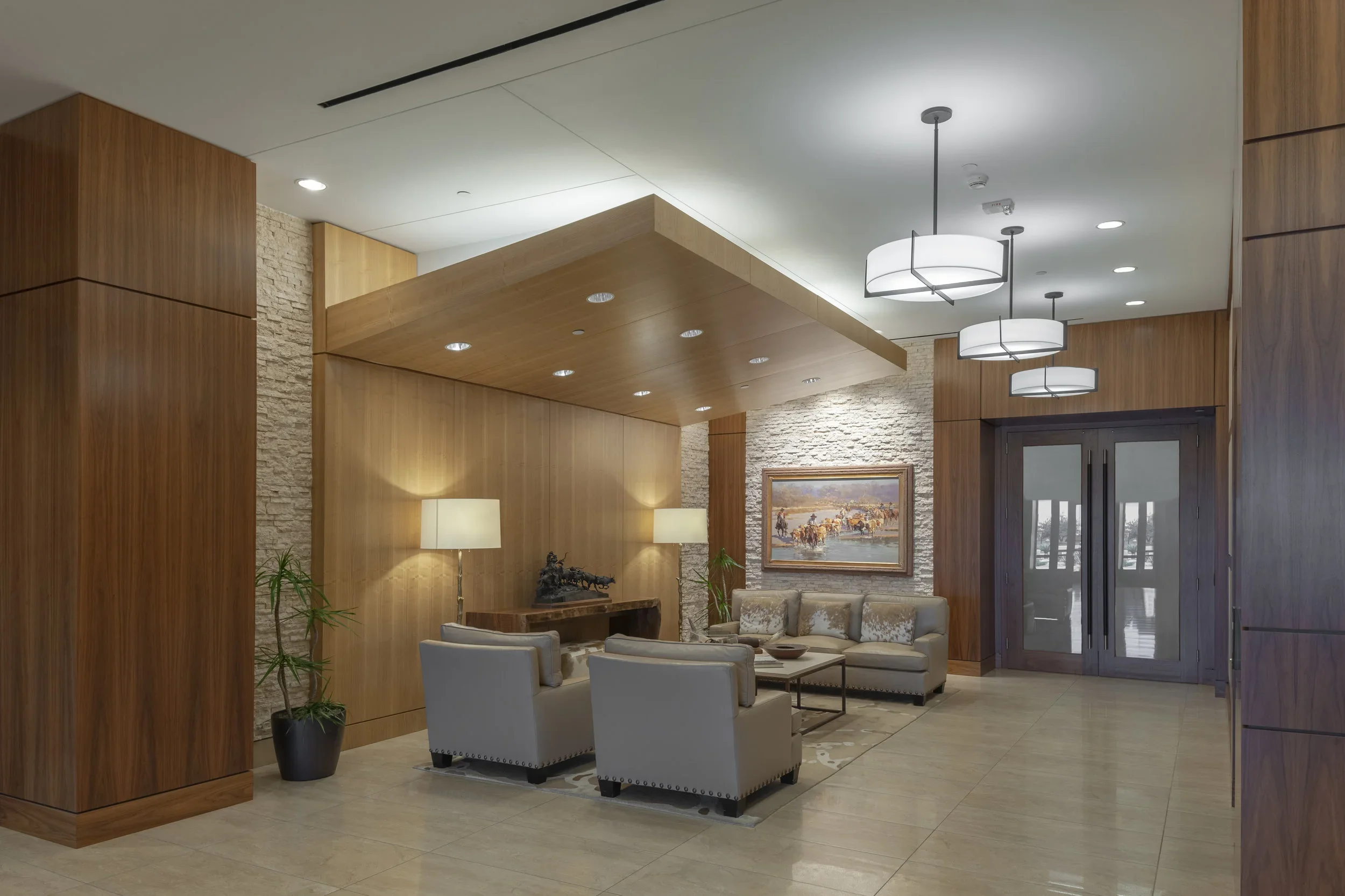 Main Lobby of EOG Midland Headquarters Building II with beige sofas, wooden panels, a stone accent wall, potted plants, a painting, and modern pendant lights.