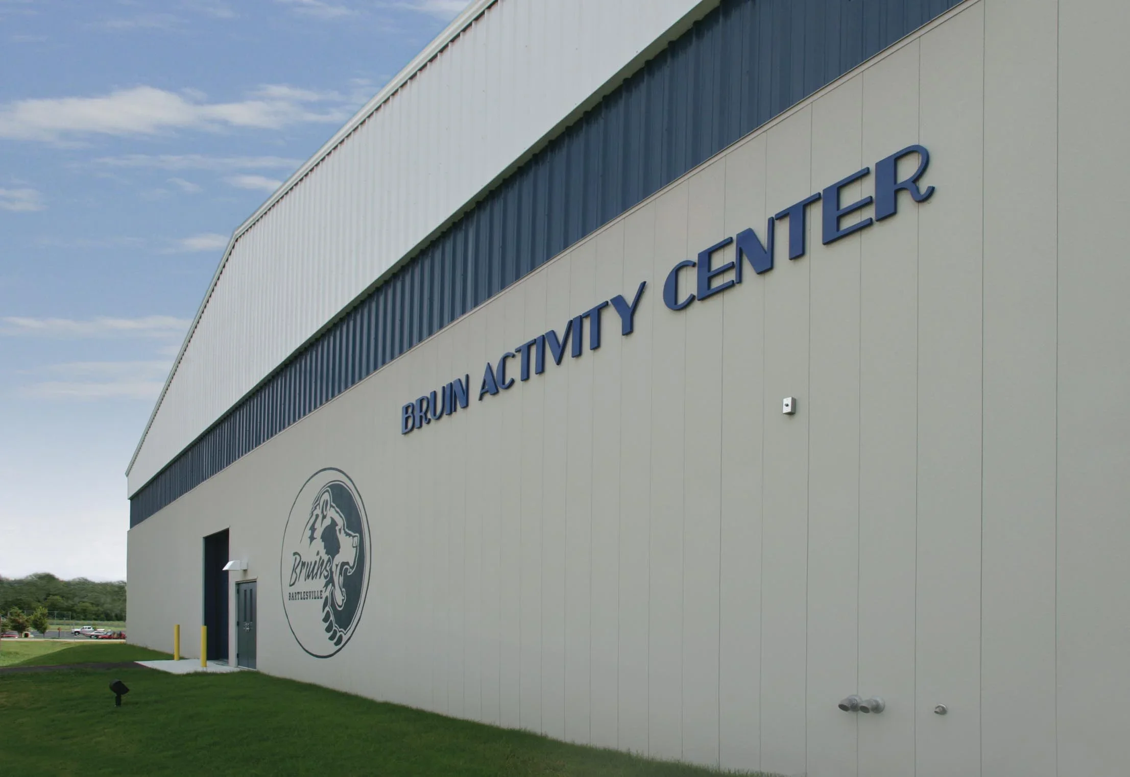 Exterior view of the Bruin Activity Center, a large gymnasium with beige walls and blue lettering, and a logo near the entrance.