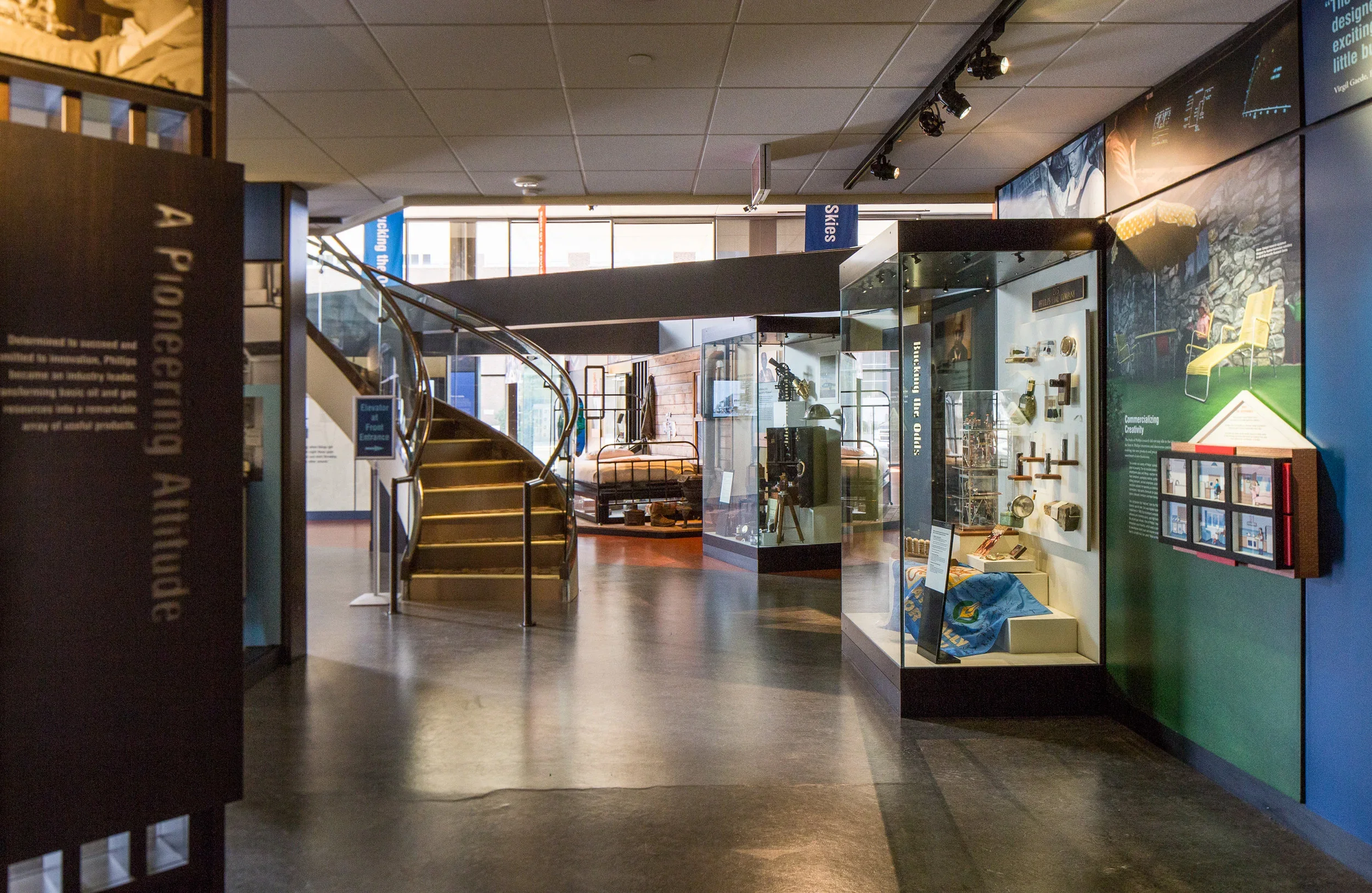 Interior of a museum exhibit space with a curved staircase, display cases with artifacts, and informational panels.