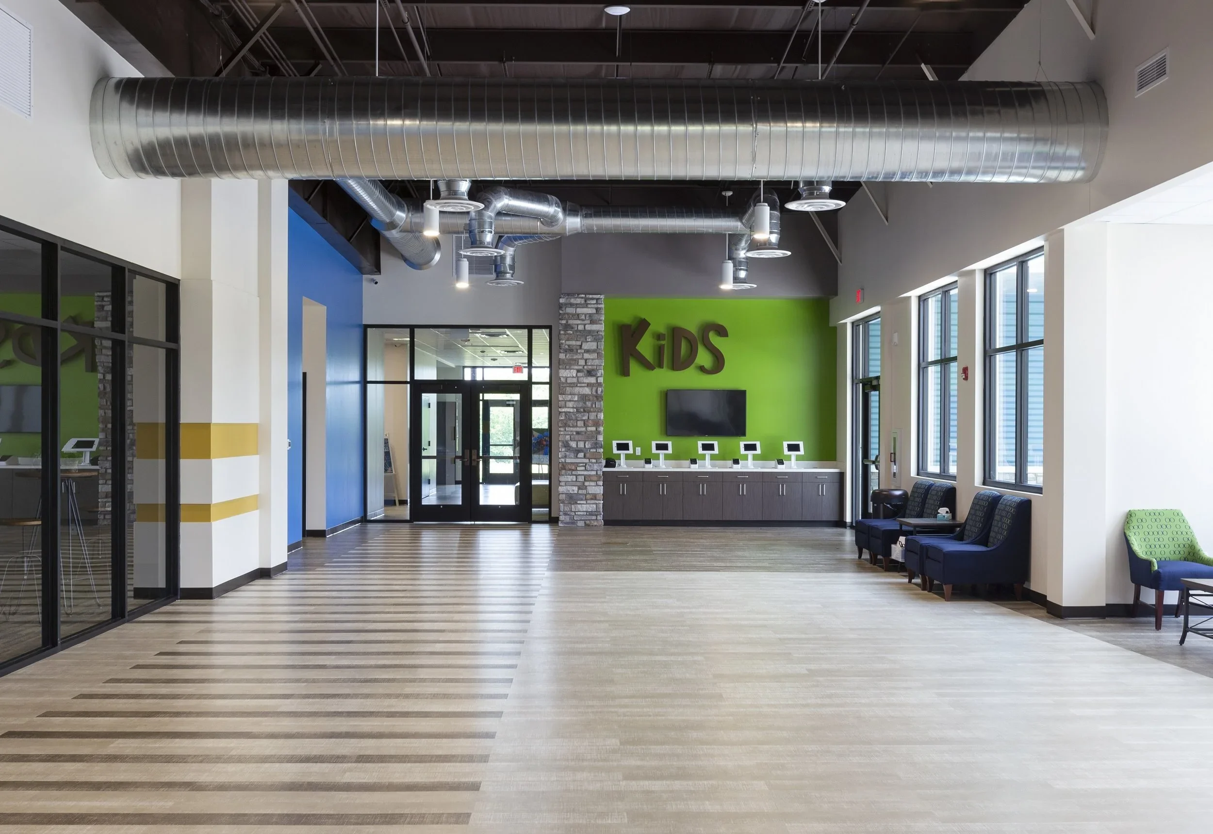 Empty lobby area with seating, windows, and a kids' play area with a green wall and television.