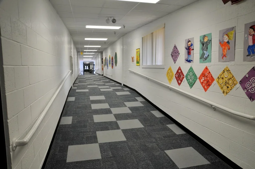 Empty hallway with colorful children's artwork and diamond-shaped decorations on white brick wall.