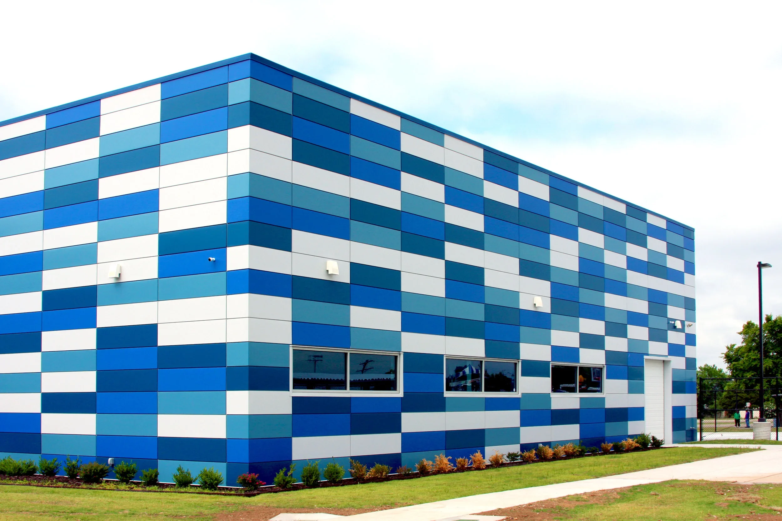 Modern building with a blue and white checkered exterior, small windows, and a white door, surrounded by a grassy lawn and sidewalk.