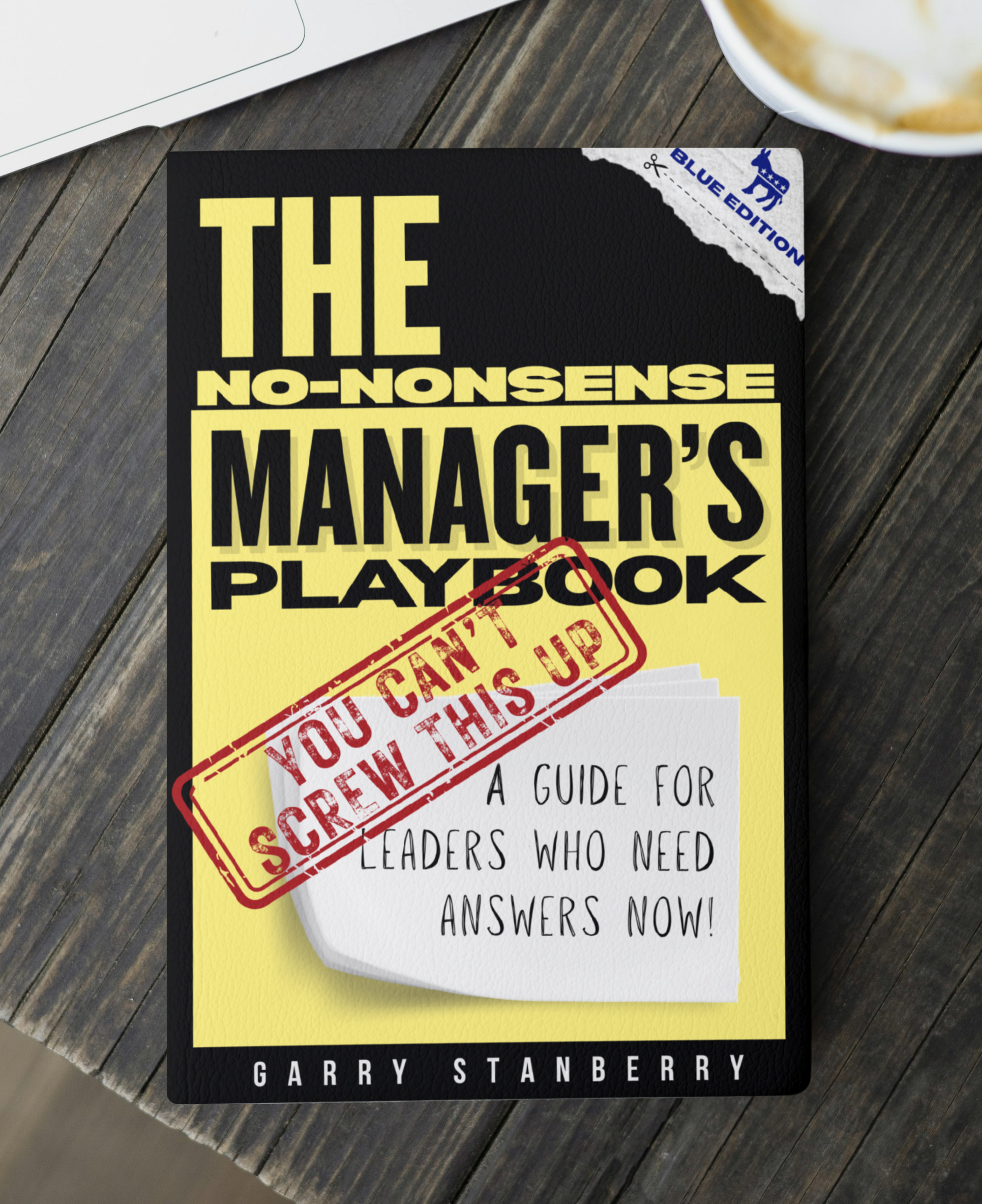 Cover of a book titled 'The No-Nonsense Manager's Playbook' by Garry Stanberry, with a red stamp overlayed that reads 'You Can't Screw This Up' and a subtitle 'A Guide for Leaders Who Need Answers Now!', placed on a wooden table next to a laptop, partially visible cup of coffee, and a notepad.