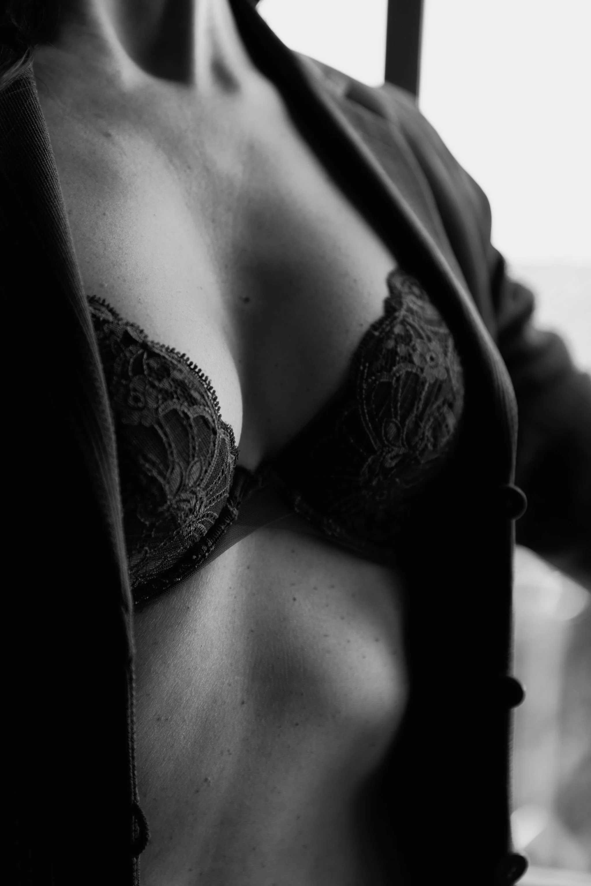 Close-up black and white photo of a woman's chest wearing a lace bra and a partially open blazer.